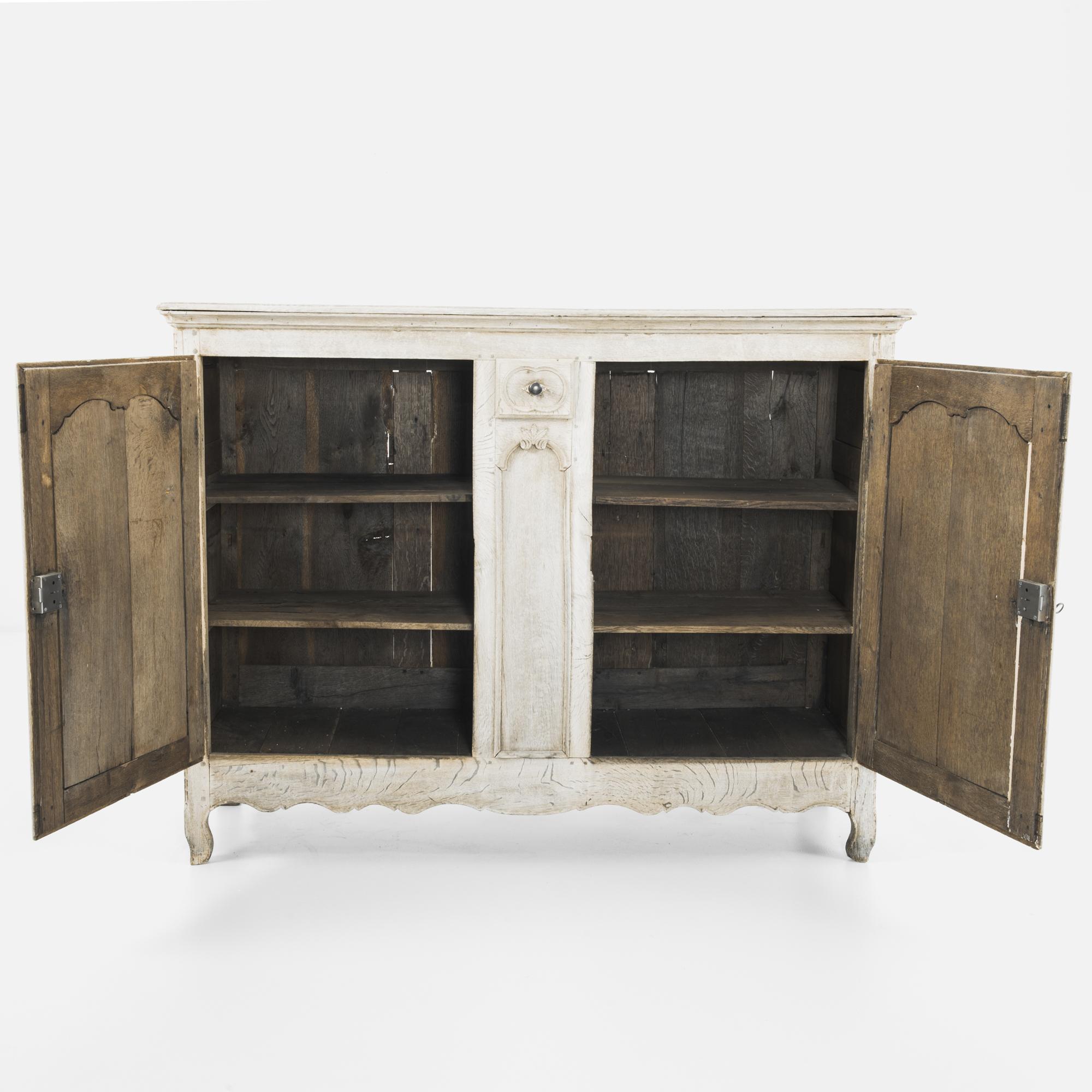 A two-door oak buffet from France, circa 1850, with a single center drawer. The upright frame is subtly embellished by the expressive raised panels on the cupboard doors and the filigree of the pulls, hinges and locks, in polished, time-worn
