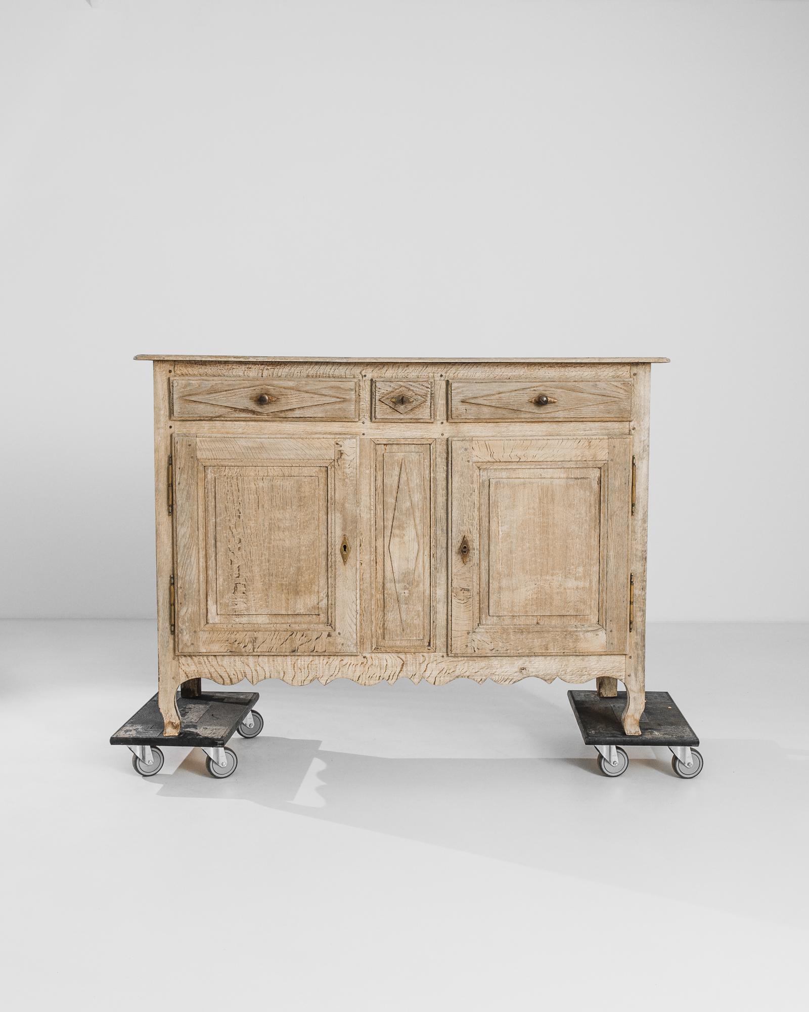An oak buffet from 1850s France. Cabriole feet and a scalloped apron lend the upright case a refined poise. Carved diamond accents on the panels of the drawers lend a graphic touch, echoed in the gilded diamond lock-pieces.The wood has been restored