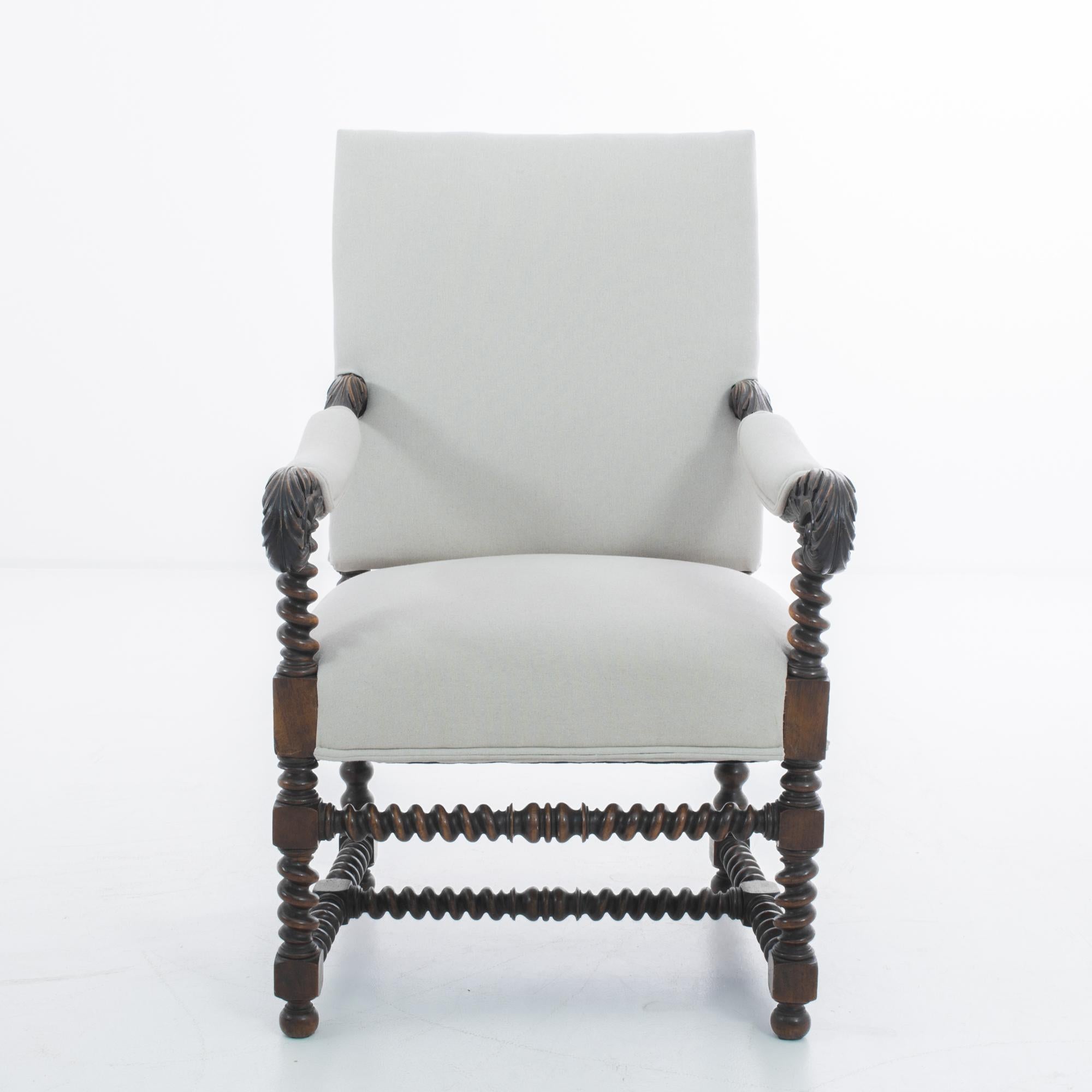 A wooden armchair from France, produced circa 1850. A regal antique, this stately armchair is newly upholstered in a grey fabric that contrasts just right with the dark stained wood. Lavishly carved with acanthus leaf armrests and barley twist