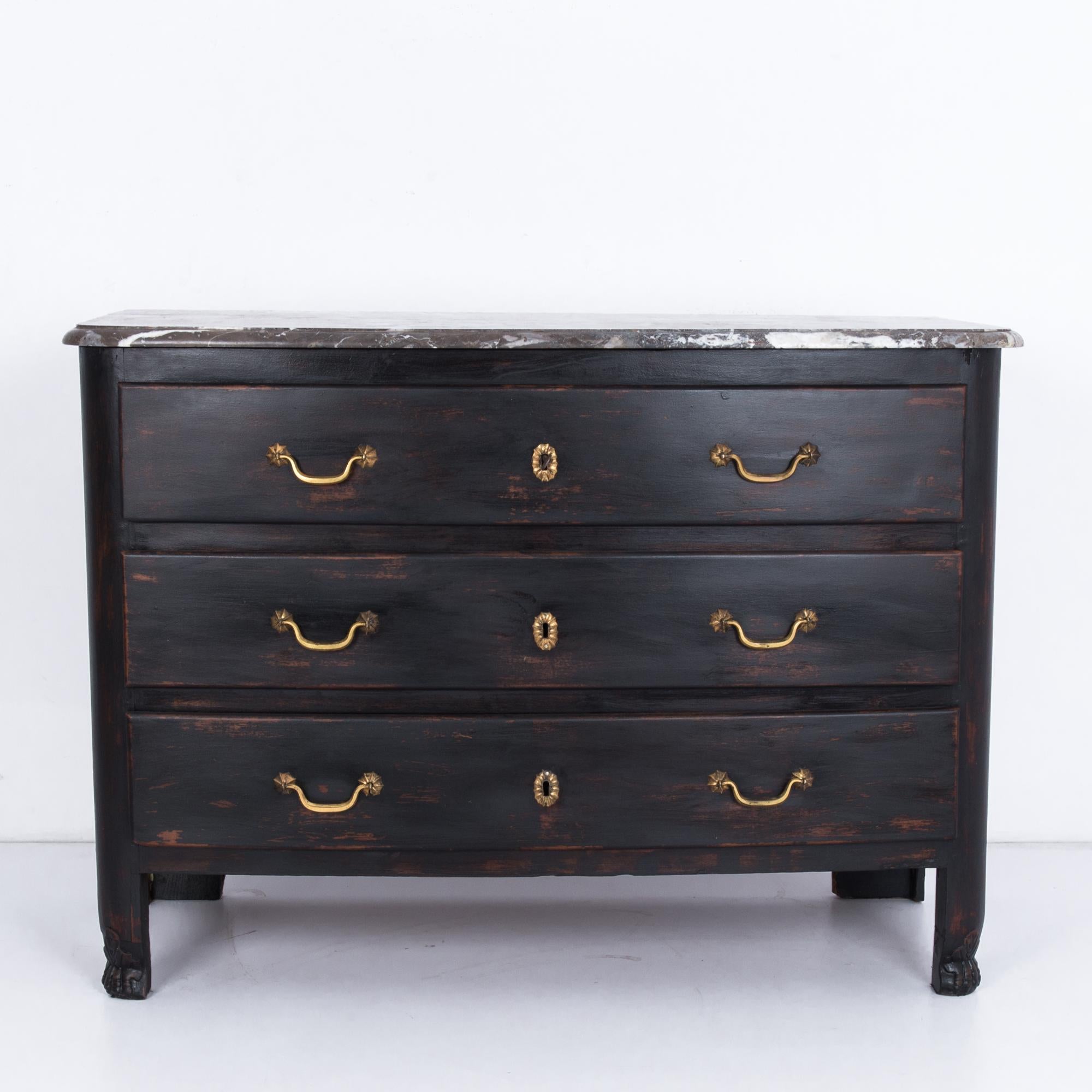 A wooden chest of drawers from France, circa 1850s, with a marble top. Three drawers pull out with gilded handles. Dark, burnished wood and curved moldings give this piece a warm tone, contrasted by the cool elegance of the white-veined marble. The