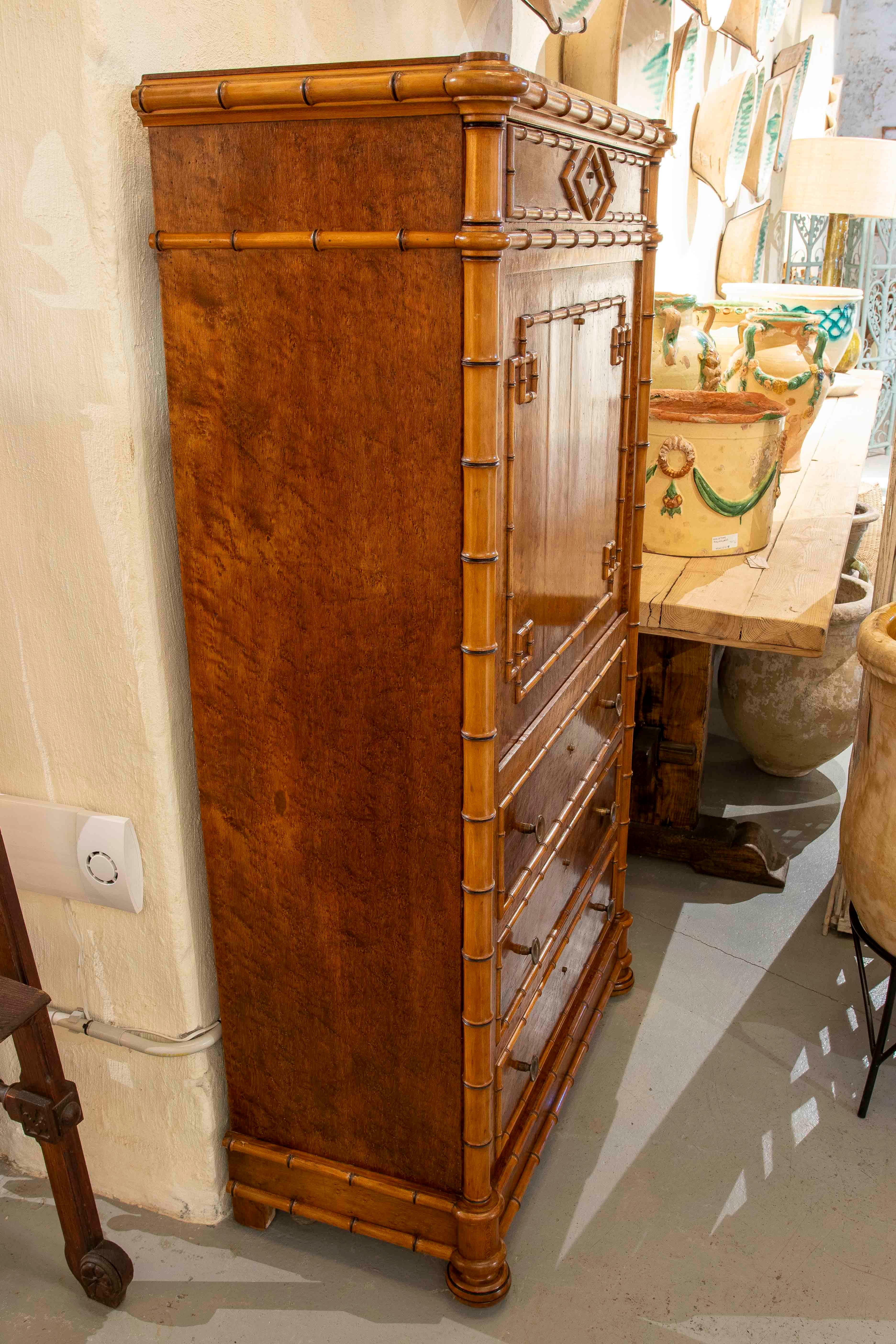 Elegante escritorio secreter vertical de inspiración Luis XVI, de madera de abedul, con marquetería de bambú en el marco y las molduras. La pieza presenta tres grandes cajones inferiores, una tapa central abatible para escribir y compartimentos