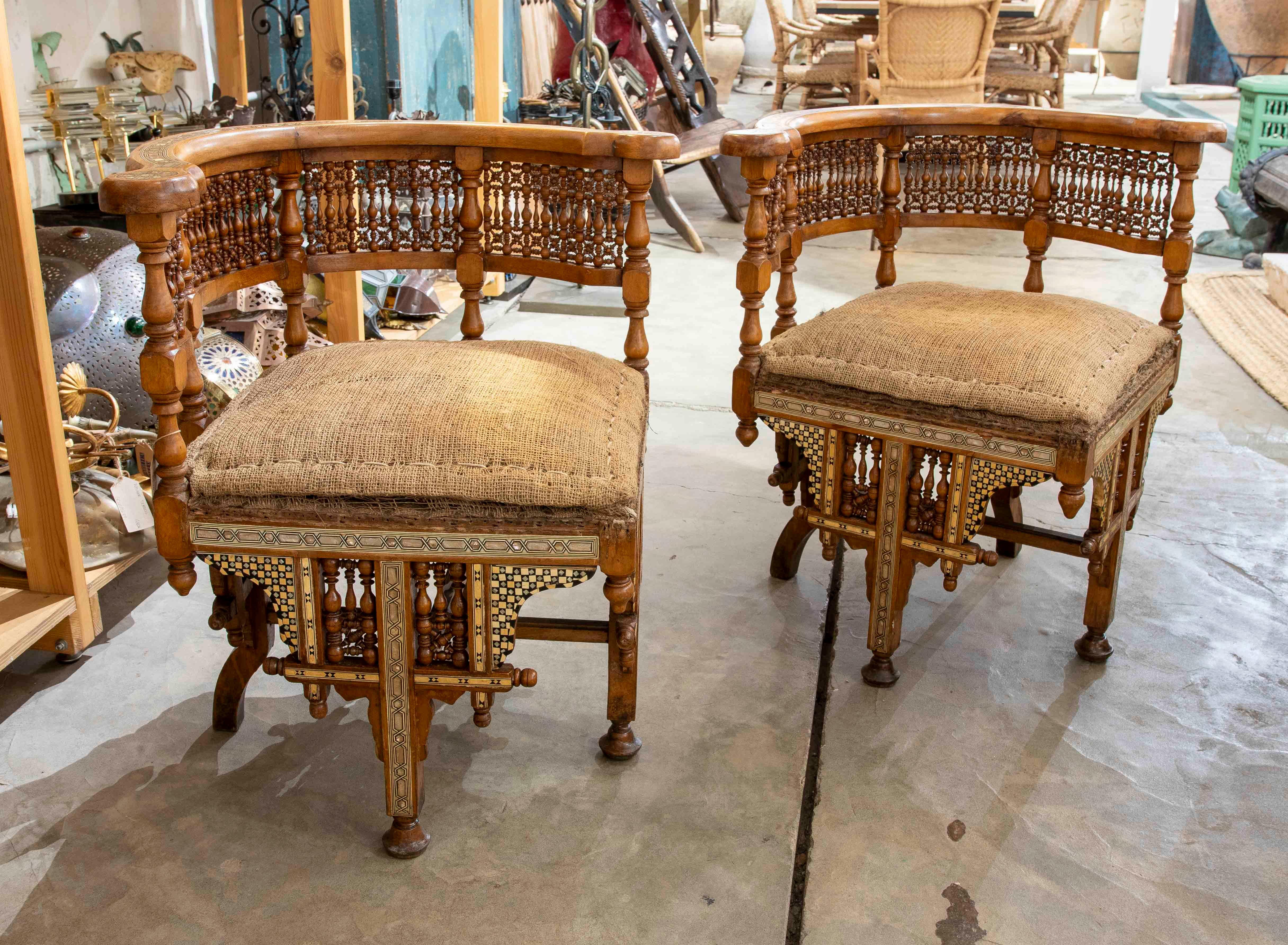 Questa elegante coppia di sedie angolari marocchine si distingue per l'intricata lavorazione del legno, una fusione unica di design coloniale britannico e influenze indiane tradizionali. La struttura curva dello schienale è impreziosita da elementi