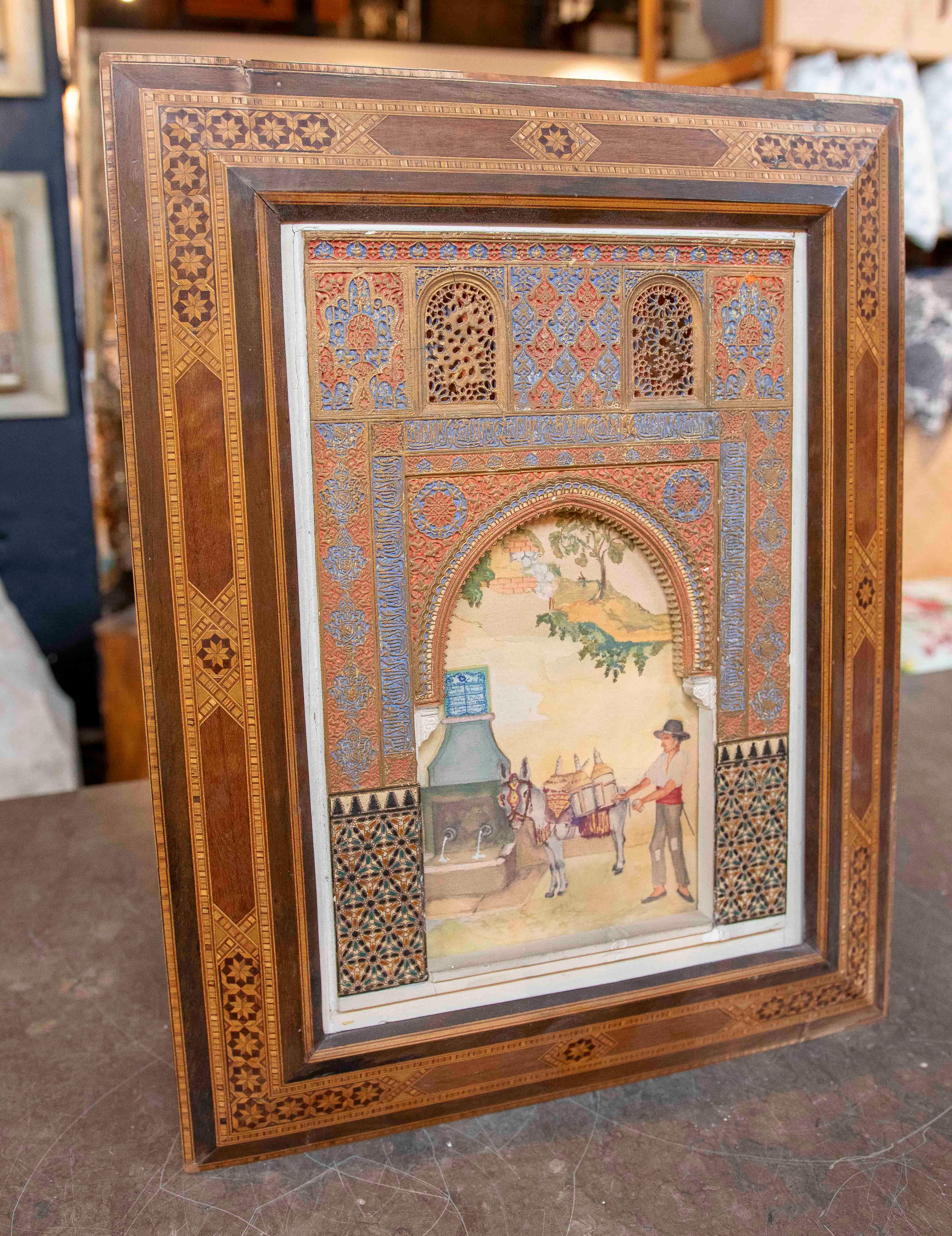 Modelo de entrada artesanal de estilo morisco con marco de madera tallada y marquetería de inspiración mudéjar, decorado con relieves policromados en tonos azules, rojos y dorados. En el interior, una encantadora escena de género representa a un