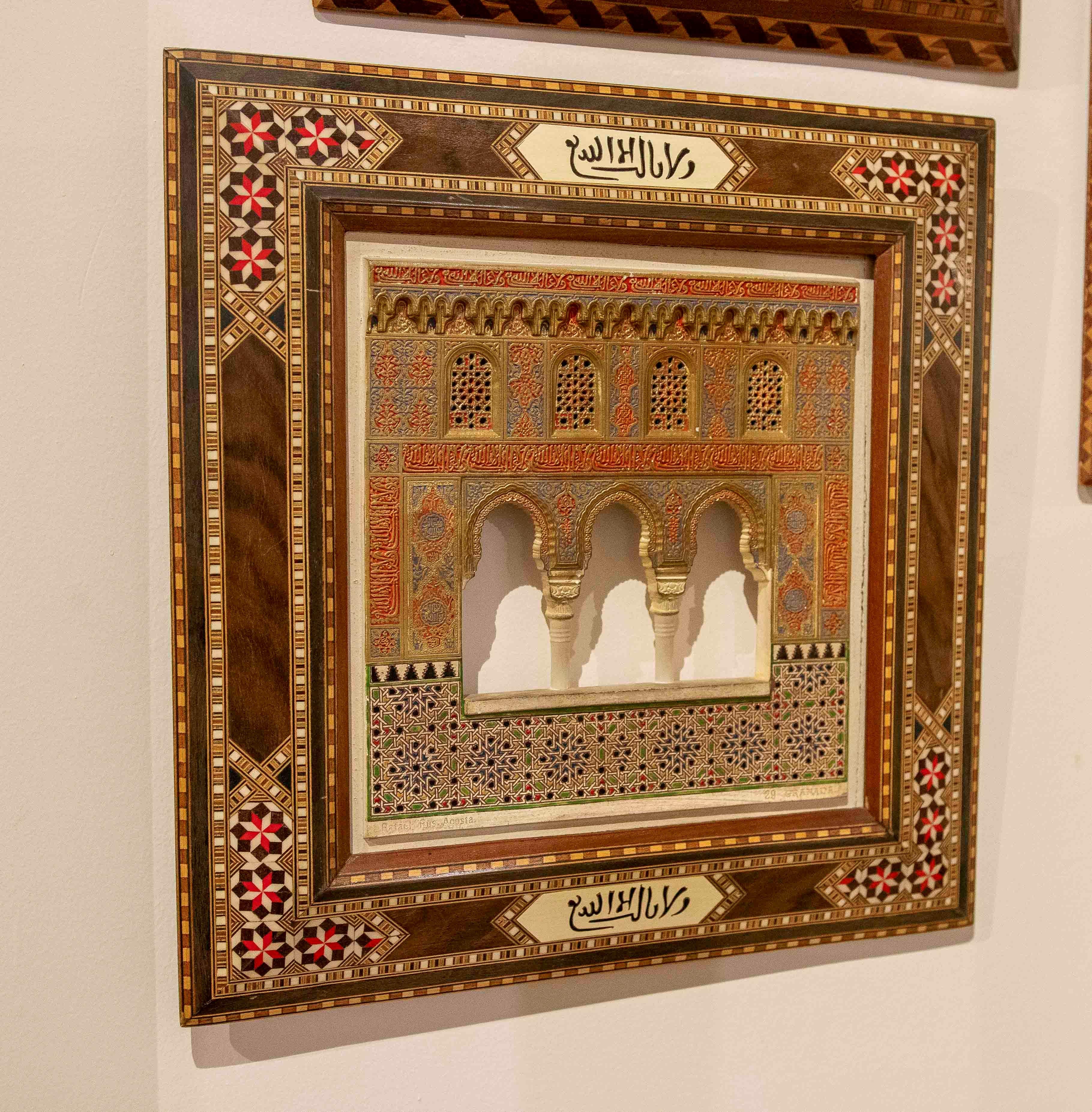 Exquis panneau en relief reproduisant une section de l'arcade de l'Alhambra de Grenade, avec de fins détails polychromes en rouge, bleu et or qui mettent en valeur la calligraphie arabe et les motifs géométriques de l'original. La partie inférieure
