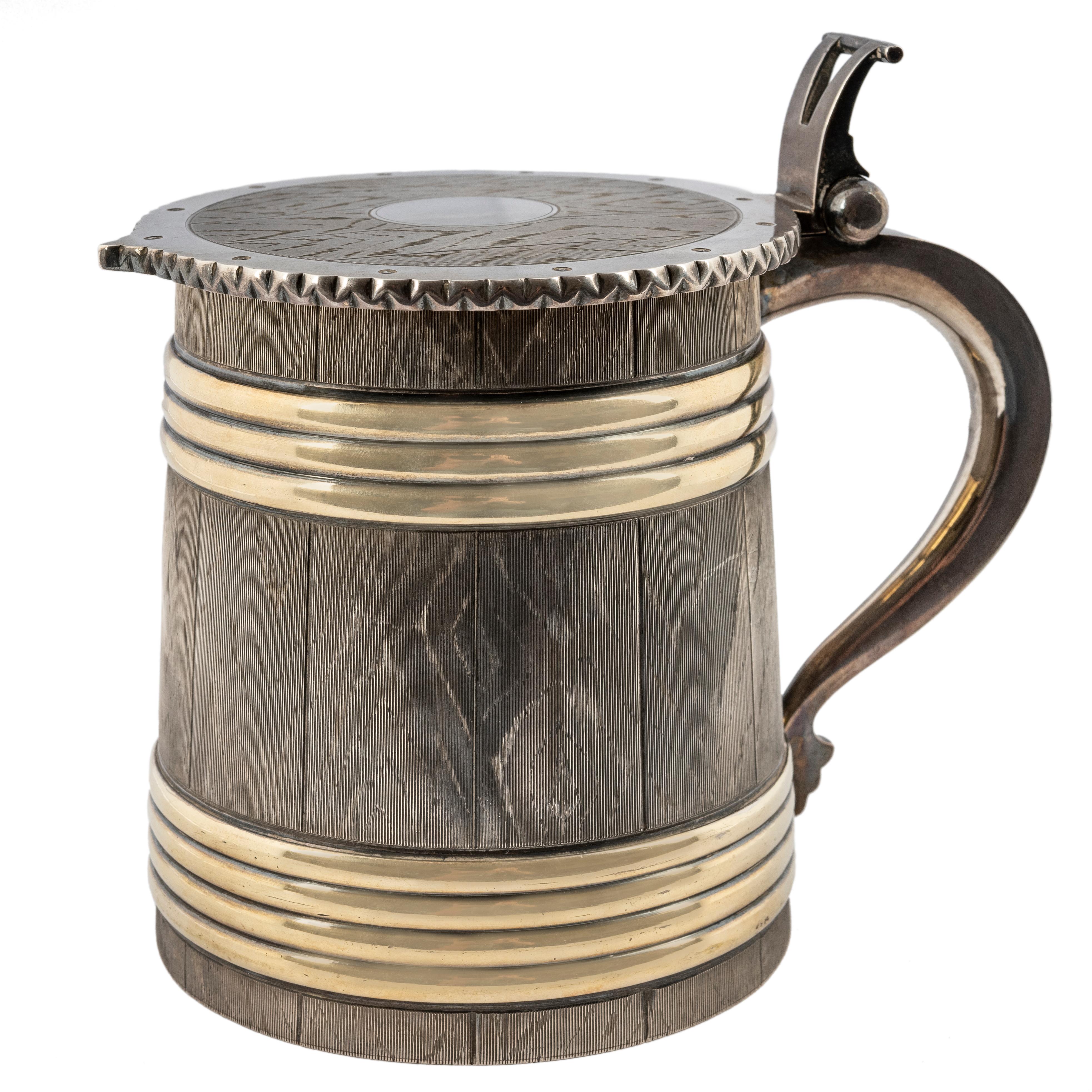 From the Romanov era, period of Tsar Alexander II, the cover and sides of the trompe l'oeil silver tankard chased to simulate oak woodgrain, enhanced with horizontal polished silver gilt bands. The hinged cover has a crenelated edge surrounding a