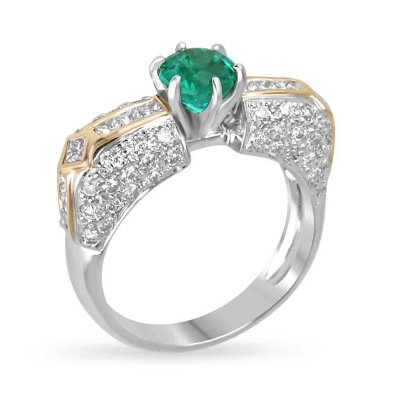 This breathtaking ring features a stunning round-cut Colombian emerald at the center, radiating a vivid rich green color and securely set in a six-prong setting. Surrounding the emerald are clusters of pave-set round-cut diamonds, with princess-cut