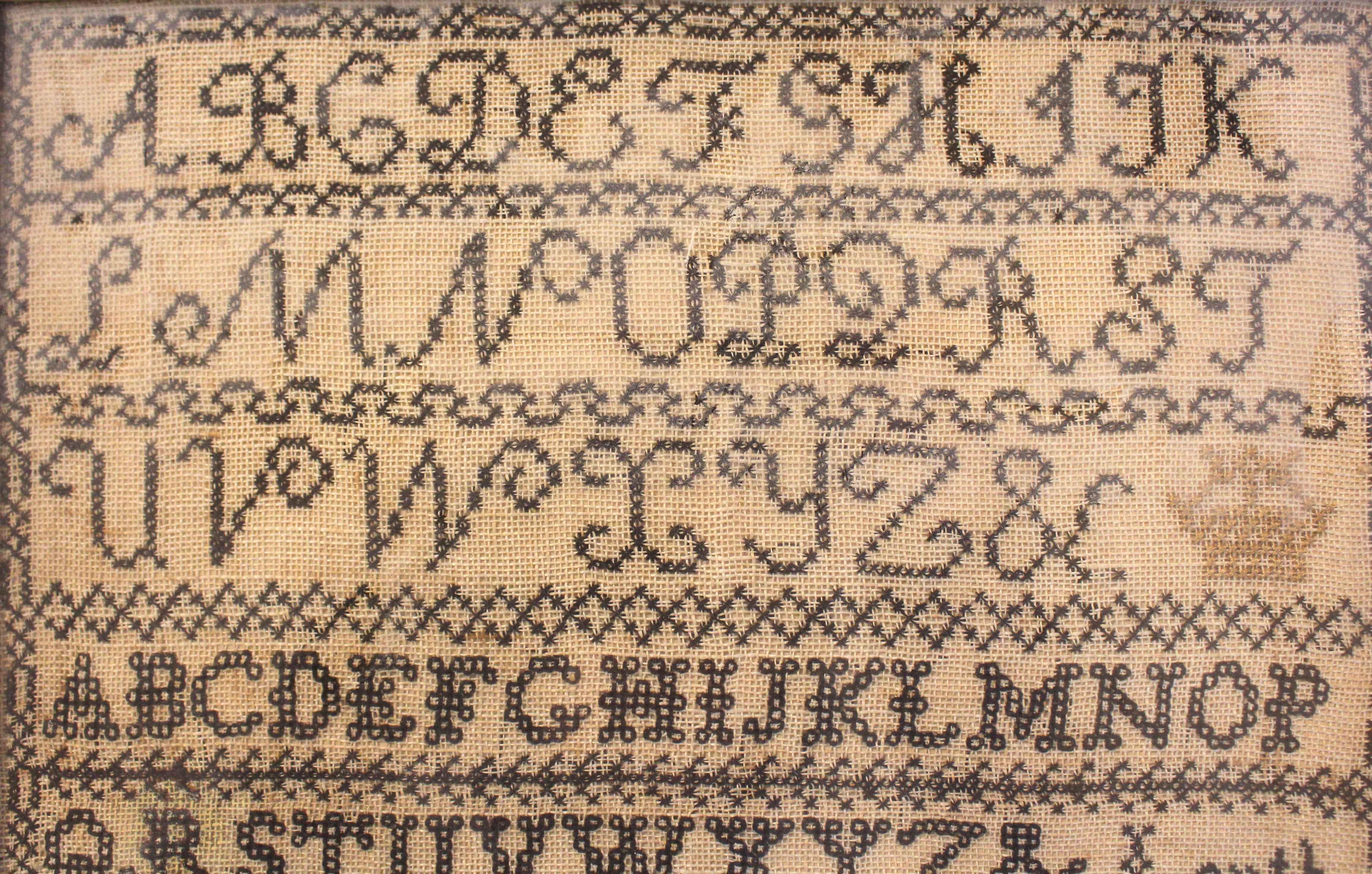1860 Sampler made by Selina Kirk in oak frame, English. Star-burst large letters & chain stitch medium letters above an urn with tulip flanked by birds in trees. Cross-stiched borders. English with an imperial crown included. In a later English 19th