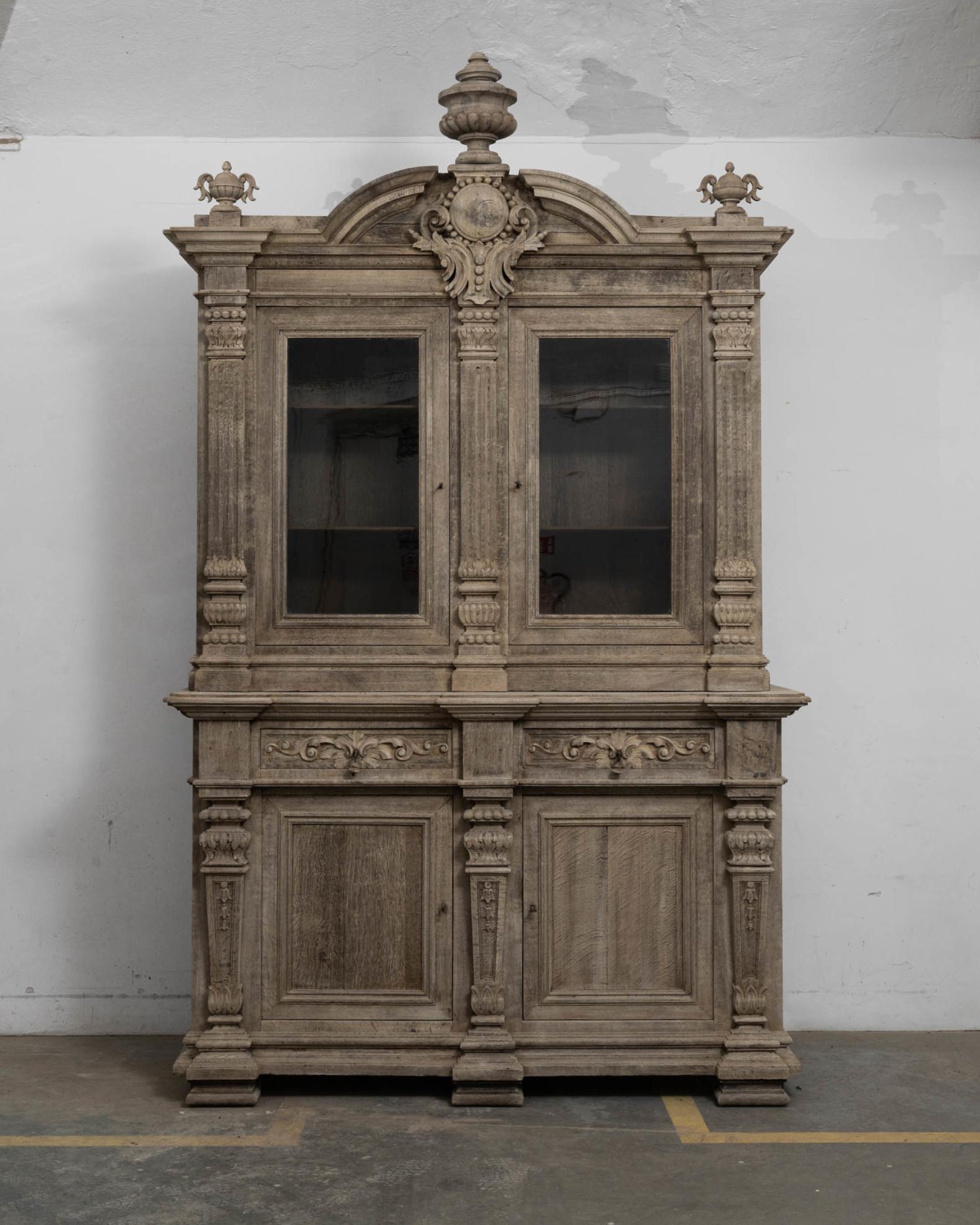 Magnificent and ornate, this antique oak vitrine cuts an impressive figure. Built in Belgium in the 1860s, the design is inspired by the elaborate furniture of the Renaissance. Beautifully carved urns crown the cabinet, evoking those found in the