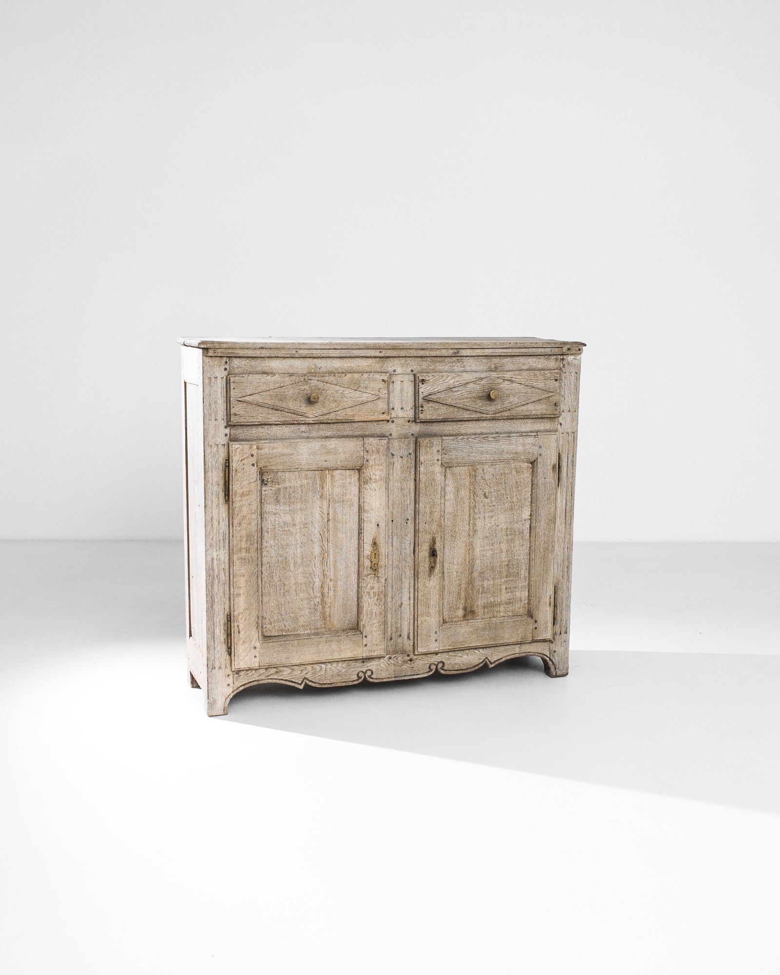 A graceful oak buffet from 1860s France. The almond tone of the oak is embellished by a gentle sanding process, revealing the natural patterns of the wood. The upright profile is contrasted by a smoothly carved scalloped apron. The diamond shapes