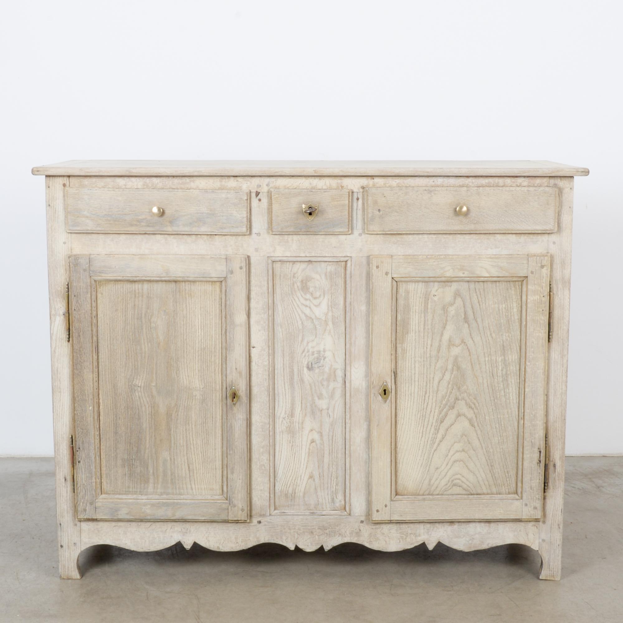 This bleached oak buffet was made in France, circa 1860. The upper section comprises a small drawer between two larger ones; the storage compartment below has two shelves. Slightly elevated on legs, the buffet features a scalloped apron. The rear