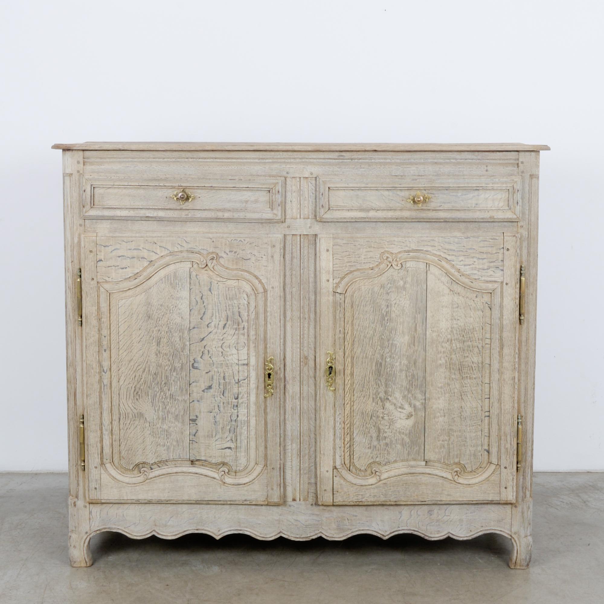 This bleached oak buffet was made in France, circa 1860. The scalloped apron and elegant curves of the paneling display the outstanding craftsmanship behind this piece. The buffet houses two drawers, and the set of double doors below open to reveal