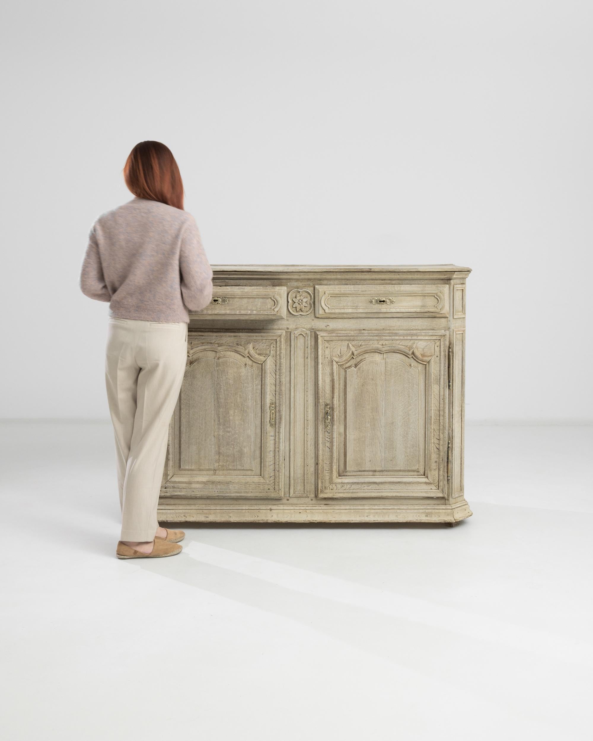 This 1860s French Bleached Oak Buffet presents a timeless charm, seamlessly combining practicality and elegance. Gracing the top are two drawers, providing convenient storage for essentials. Below, two doors open to reveal shelves on each side,