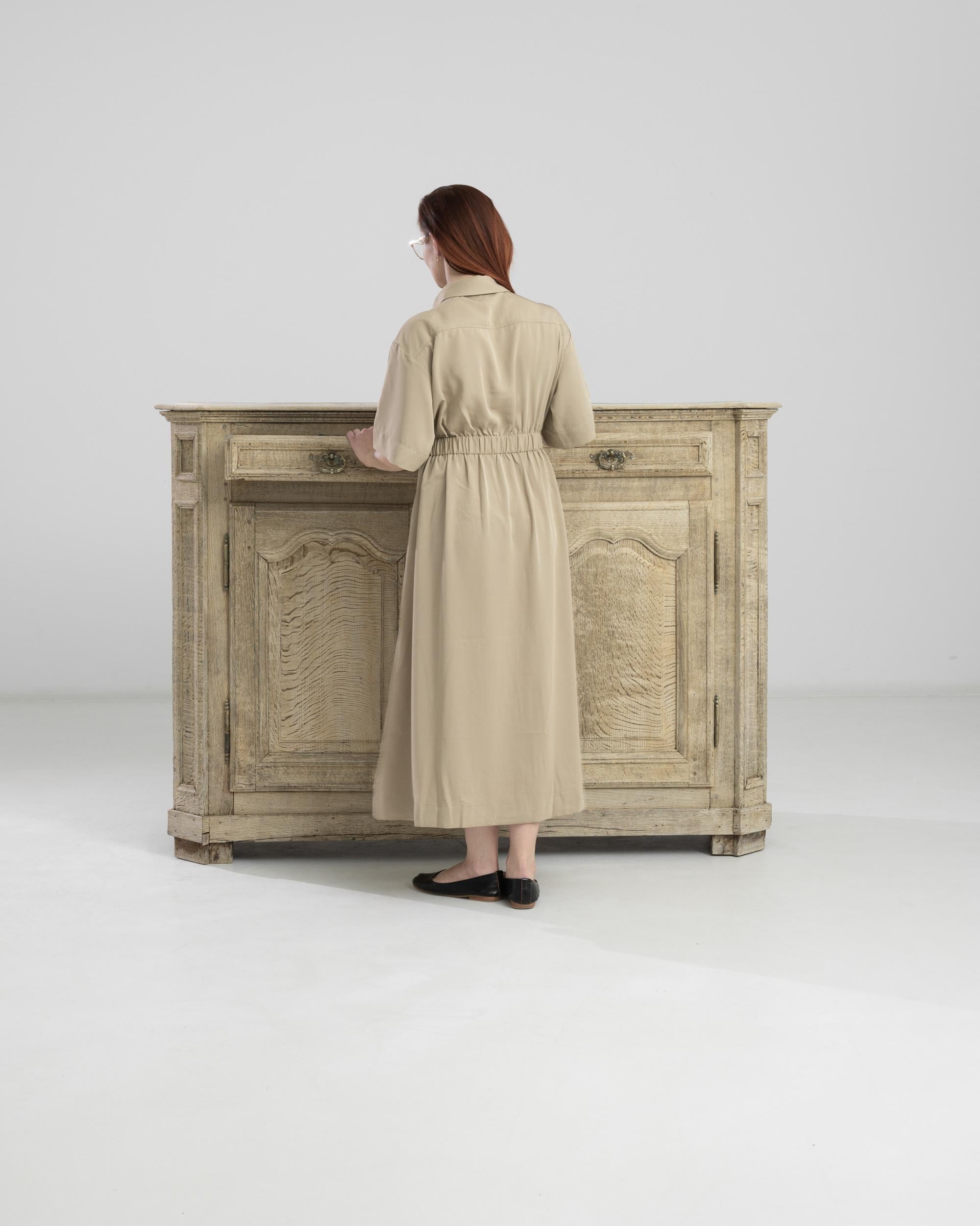 This 1860s French Bleached Oak Buffet presents a timeless charm, seamlessly combining practicality and elegance. Gracing the top are two drawers, providing convenient storage for essentials. Below, two doors open to reveal shelves on each side,