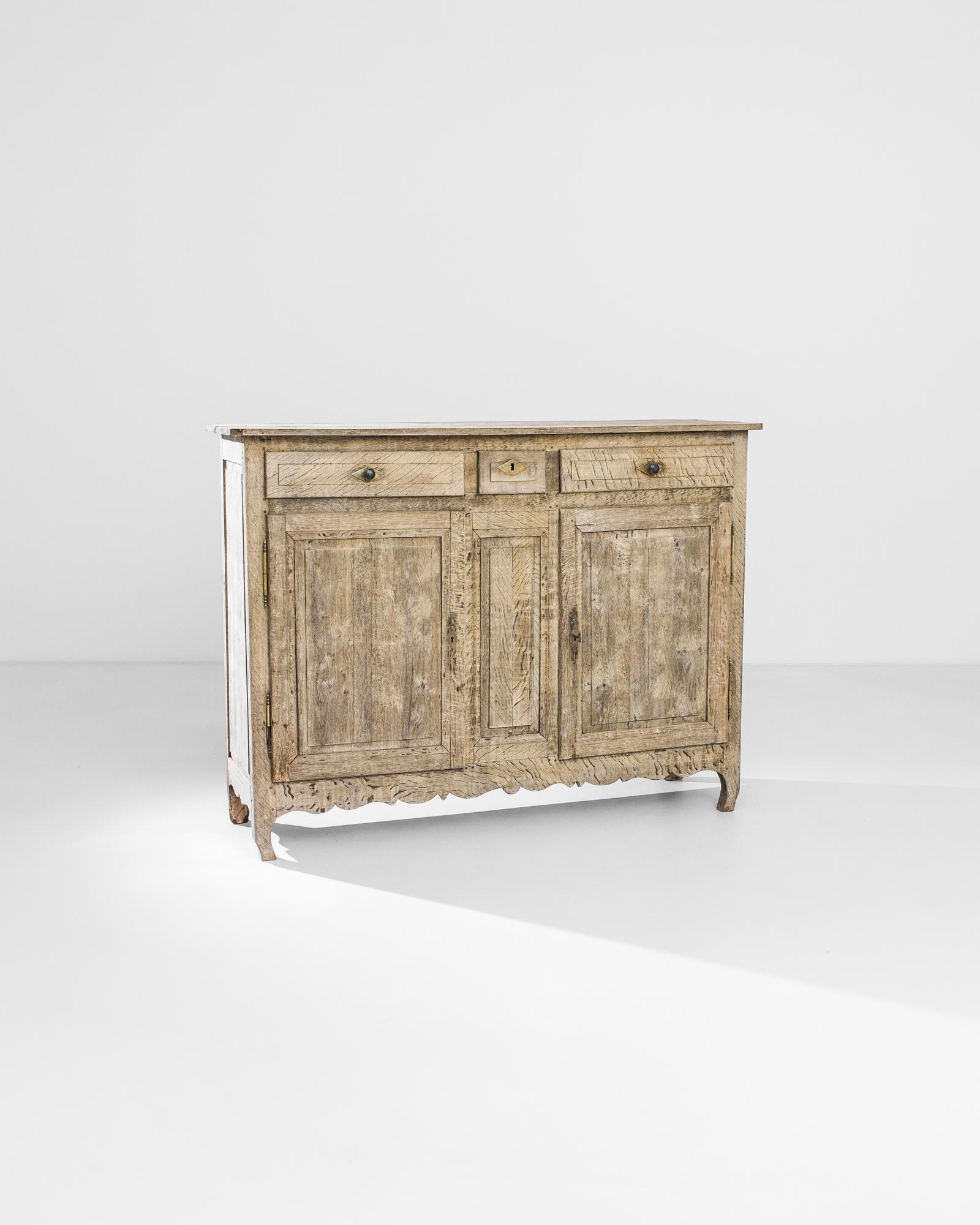 A bleached oak buffet from France, produced circa 1860. This french country style cabinet, features three sliding drawers, a locking double cabinet of two shelves, and squat cabriole front legs. A prominent wood grain takes centerstage as the main