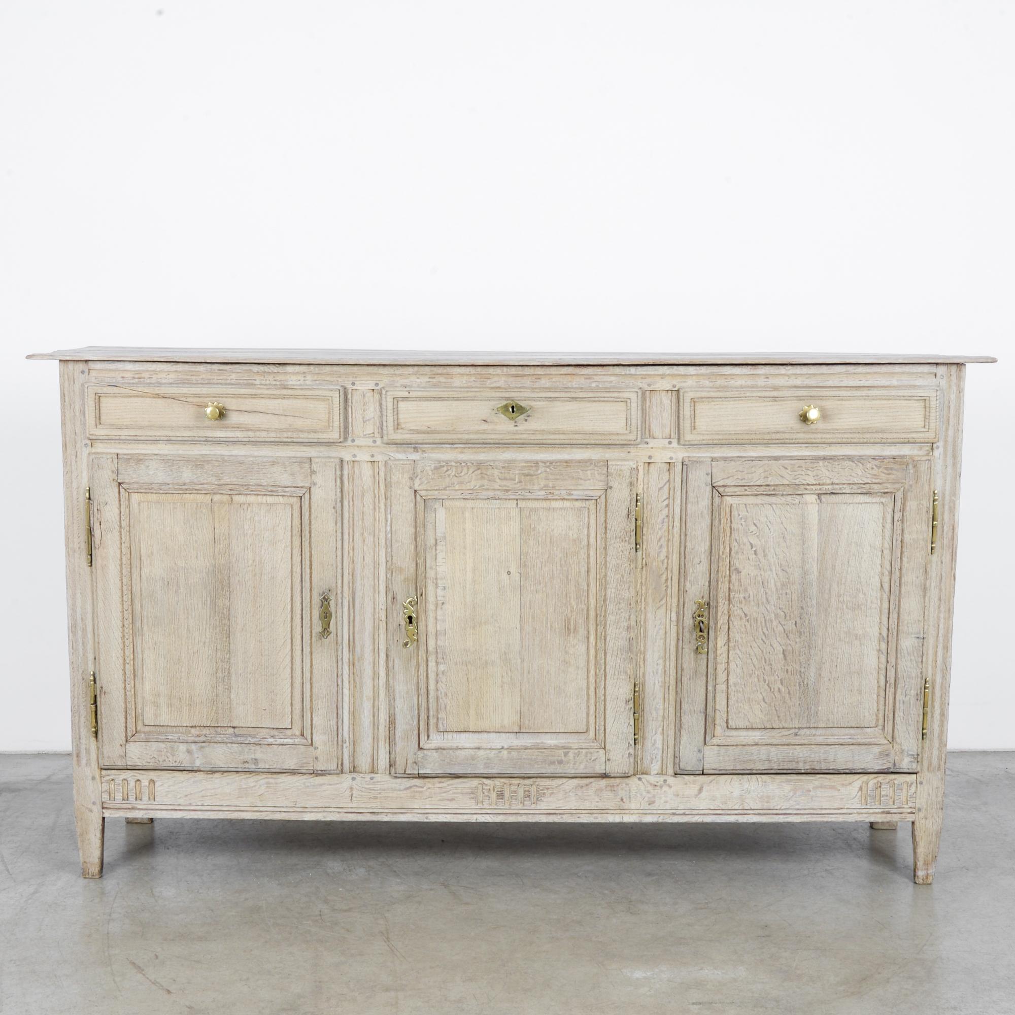 An oak buffet from France, circa 1860. Three paneled doors open onto an interior shelf; above, three pull-out drawers sport gilded knobs, framed by small sunbursts, and a diamond-shaped lock piece. The wood has been restored to the color of warm