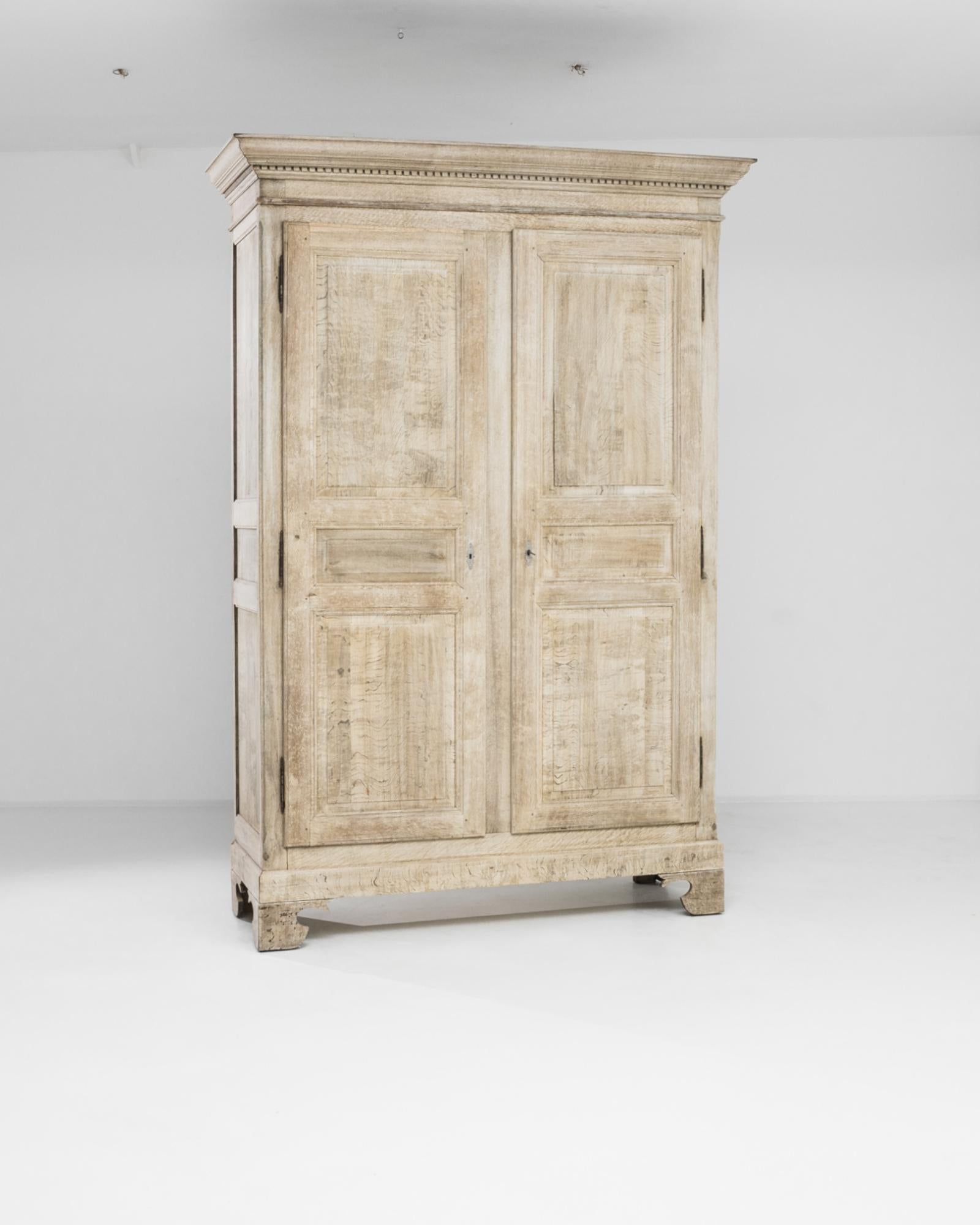 A bleached oak cabinet from France, produced circa 1860. A titan of a chest, standing just over eight feet tall, this antique double door cabinet features a cavity of four shelves held off the ground on four short corner feet, secured with metal