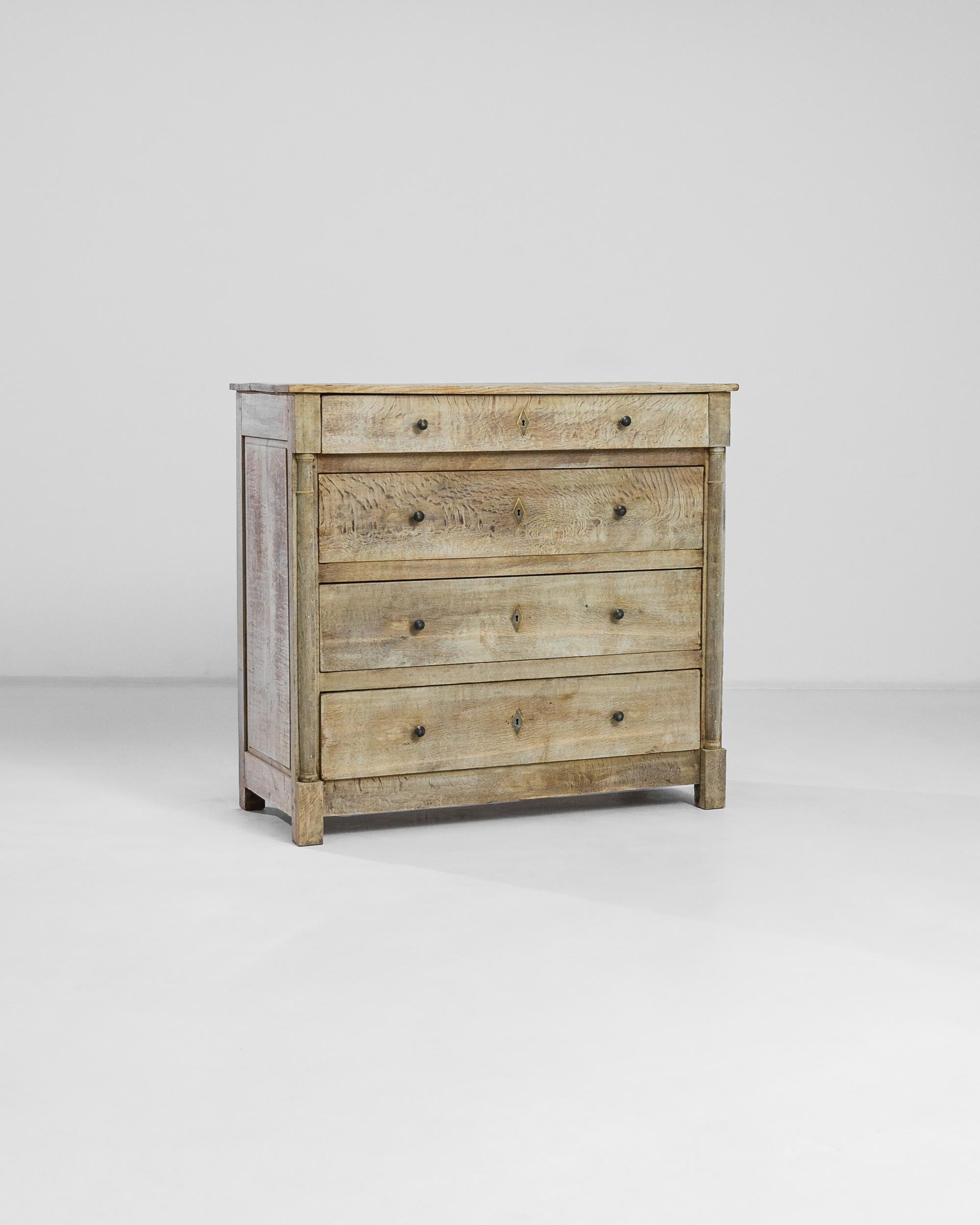 With a set of four composed drawers, this 1860s French bleached chest displays a pensive refinement. Seemingly perfectly preserved by time, its oak grain echoes like tiger stripes across its smooth surfaces. Fit with restrained brass finishings and