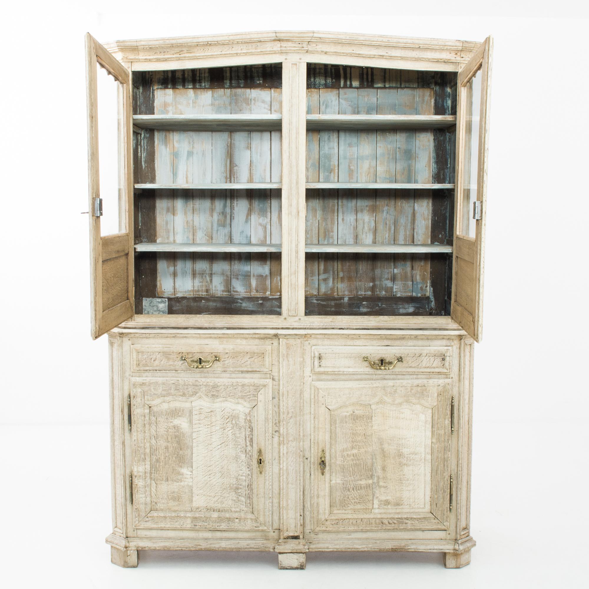 Fabriquée en France vers 1860, cette armoire en chêne blanchi présente un sommet en pente douce orné d'une moulure en couronne. La vitrine supérieure avec un cadre de fenêtre festonné offre quatre étagères et présente un intérieur peint en blanc