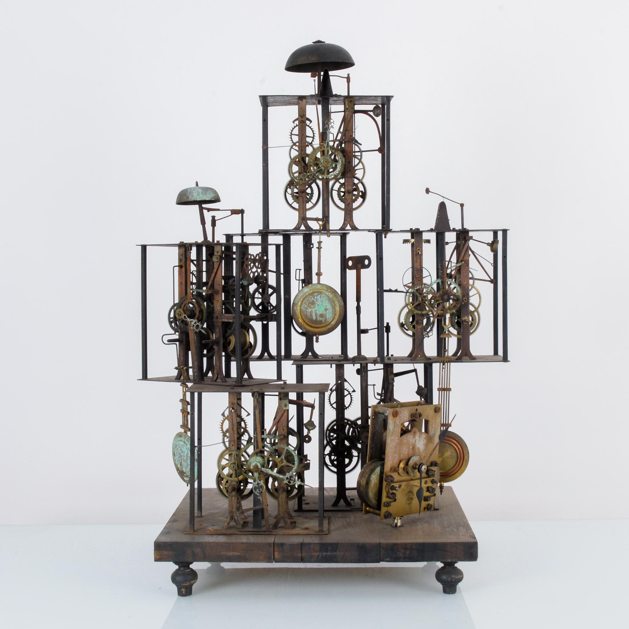 A metal clock sculpture from France, assembled from 19th century clock mechanisms. This curious assemblage rests on a wooden plinth supported by four ball feet. A dozen plus clock skeletons welded into a steampunk monument to Time stood still. A