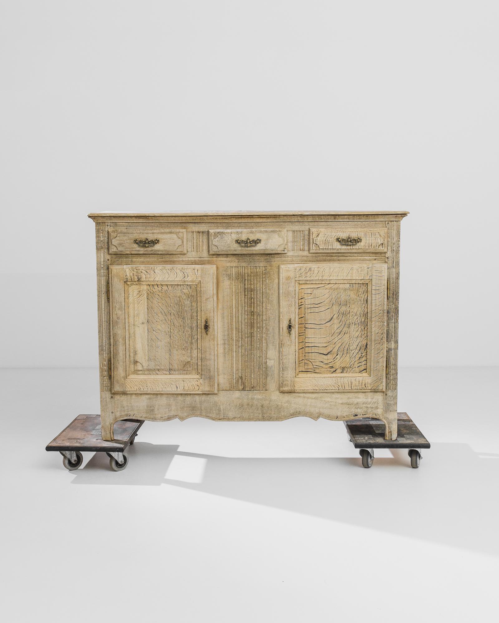 A handsome oak buffet from 1860s France, elevated upon cabriole feet. Carved accents — fluted panelling and a delicate pattern of mermaid scales on the lower corners — add subtle decorative touches, while elaborate gilded drawer handles provide a