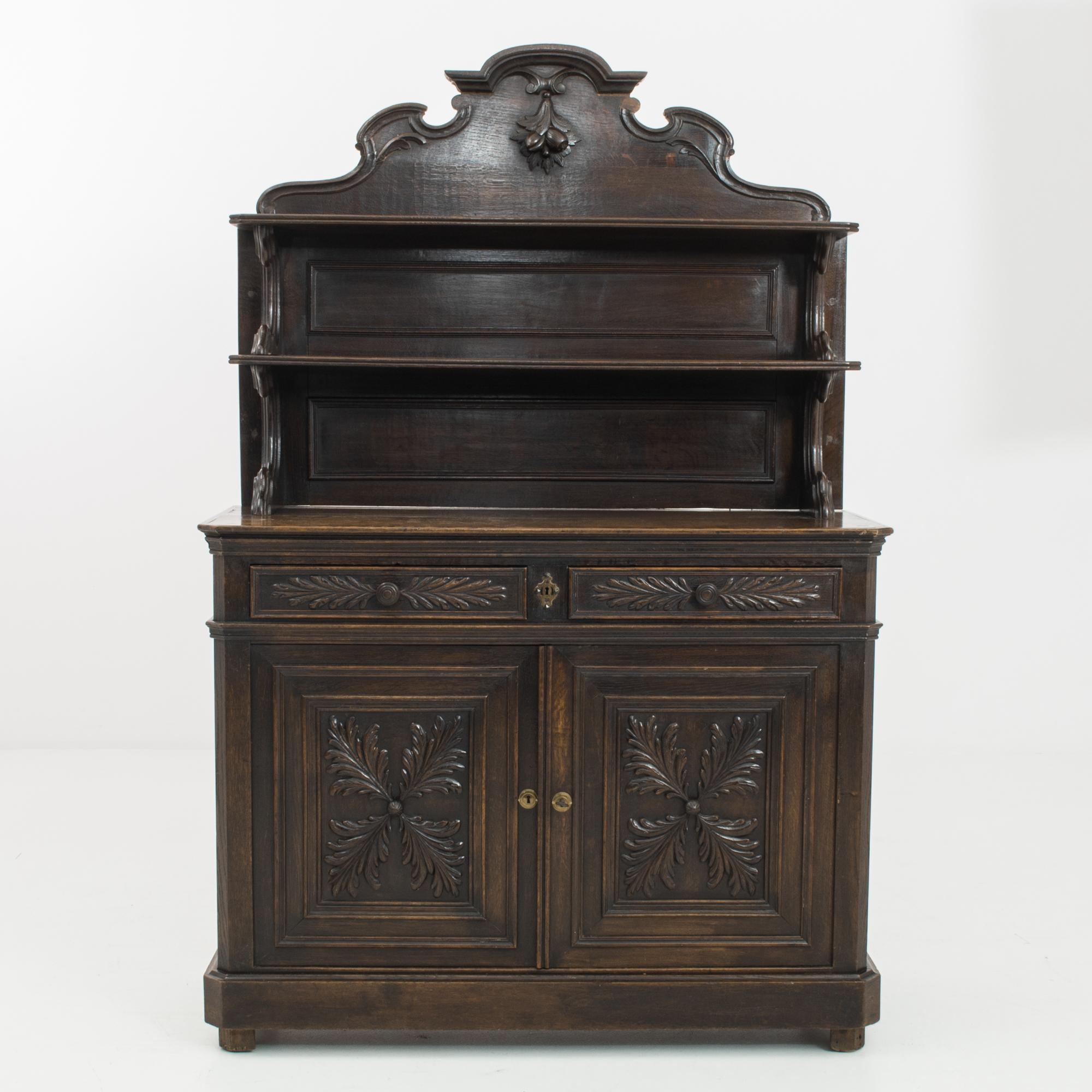 This oak cabinet was made in France, circa 1860. The remarkable workmanship behind this piece is evident in the refined floral and foliage carvings and impressive ornamented crest. Display shelves above are supported by elegantly curved brackets,