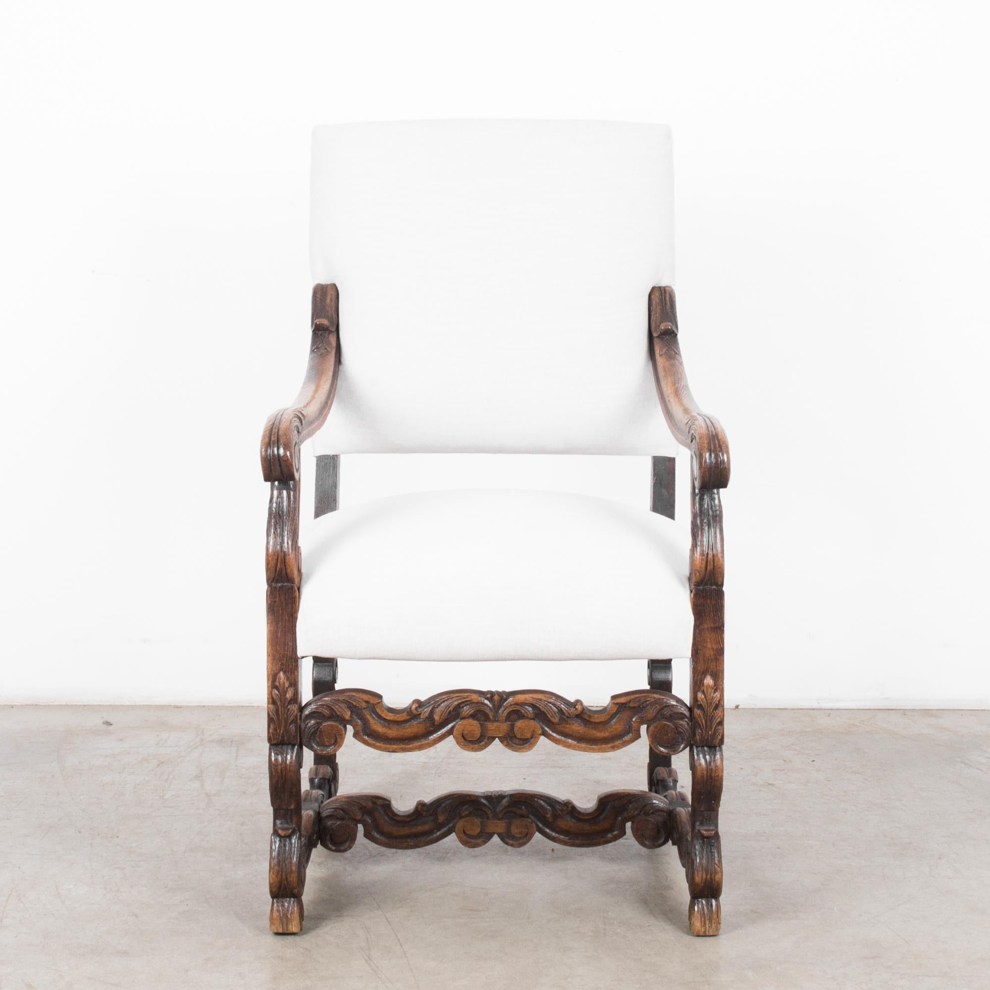 A carved wooden armchair from France, circa 1860, with an upholstered seat and backrest. The upright frame of dark, softly polished wood is carved with distinctive acanthus leaf motifs. Leafy scrolls and unfurling foliage, the slope of the carved
