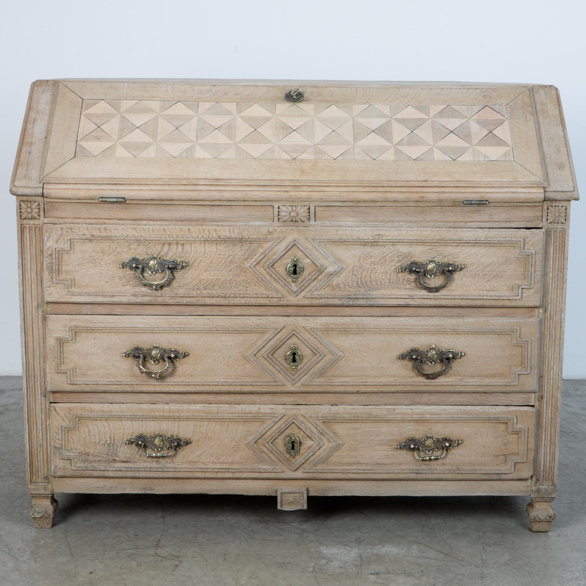 From France, circa 1860, this piece follows the tradition of French Provincial furniture workshops. With a characteristic fusion of styles. A three drawer chest supports an unfordable writing desk, in oak. The desk front panel inset with parquetry