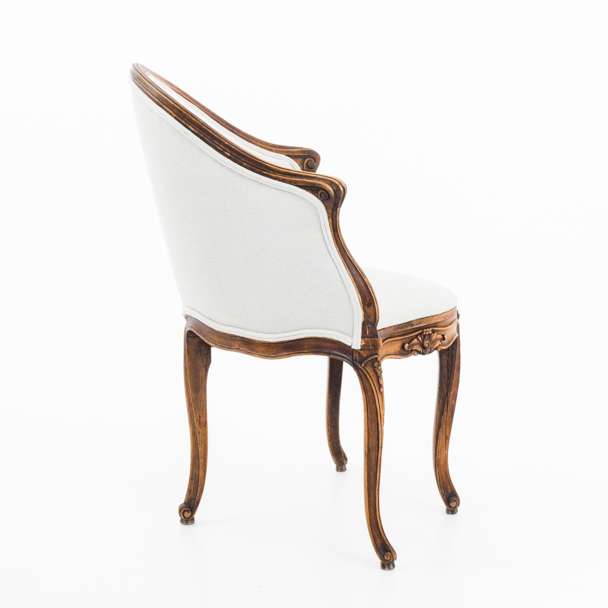 This wooden armchair with a curved backrest was made in France, circa 1860. The white upholstered seat and back accentuates the polished patina, which displays a radiant hue deepened over time. Cabriole legs and carvings of flowers and scrolls make