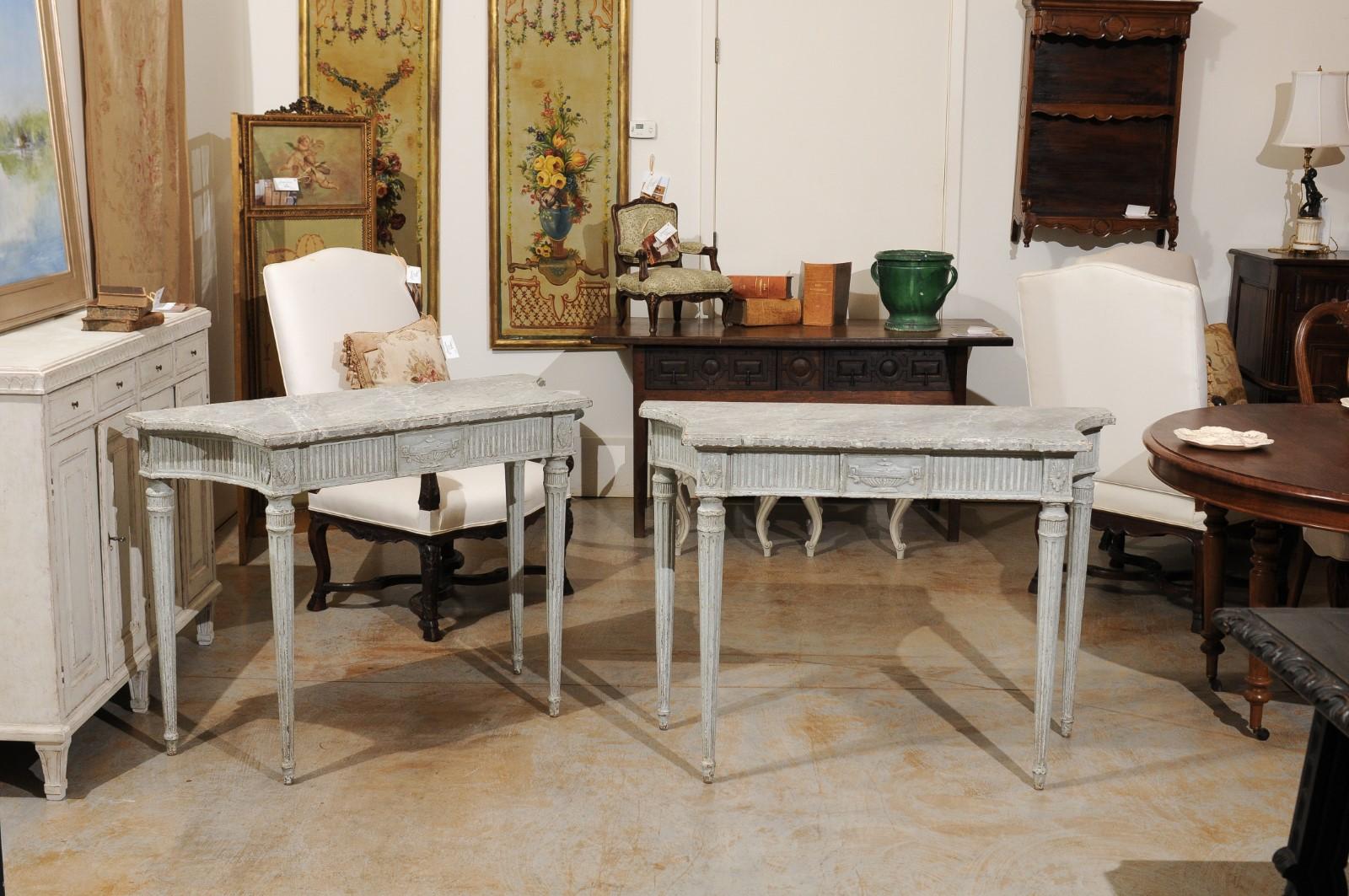 Two French Louis XVI style painted and console tables from the third quarter of the 19th century with curving faux-marble tops, reeded aprons, carved vases and fluted legs. The tables are priced and sold individually. Born under the reign of