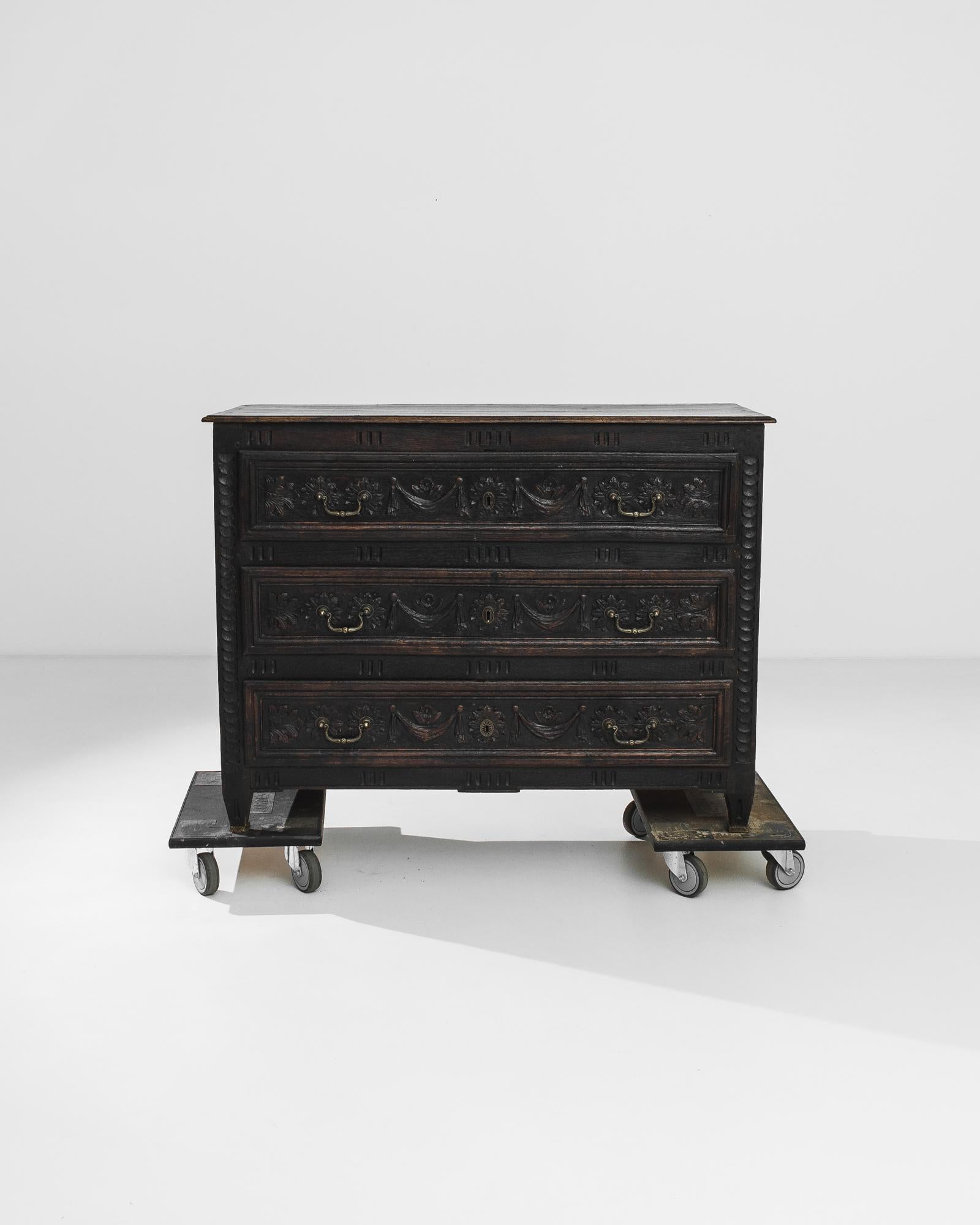 The rich, dark tone of the original patina gives this antique chest of drawers a solemn beauty. Made in France in the 1860s, the panels of the drawers are decorated with lush carving. Motifs of petalled rosettes, acanthus leaves and hanging
