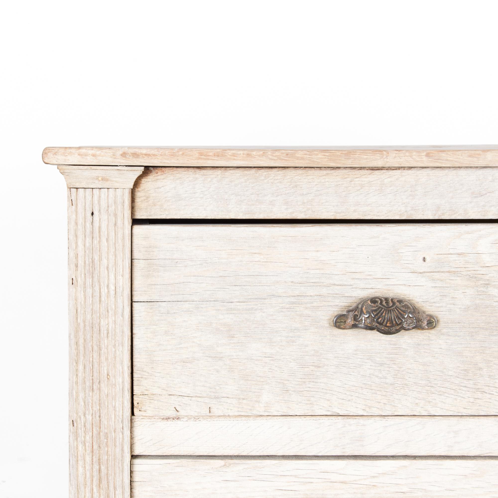 A chest of drawers from France, circa 1860, in brightly finished oak. Three drawers sport original handles and lock pieces, made of a dark, patinated brass. Square fluted column moldings evoke a neoclassical sensibility. Cup handles are embellished