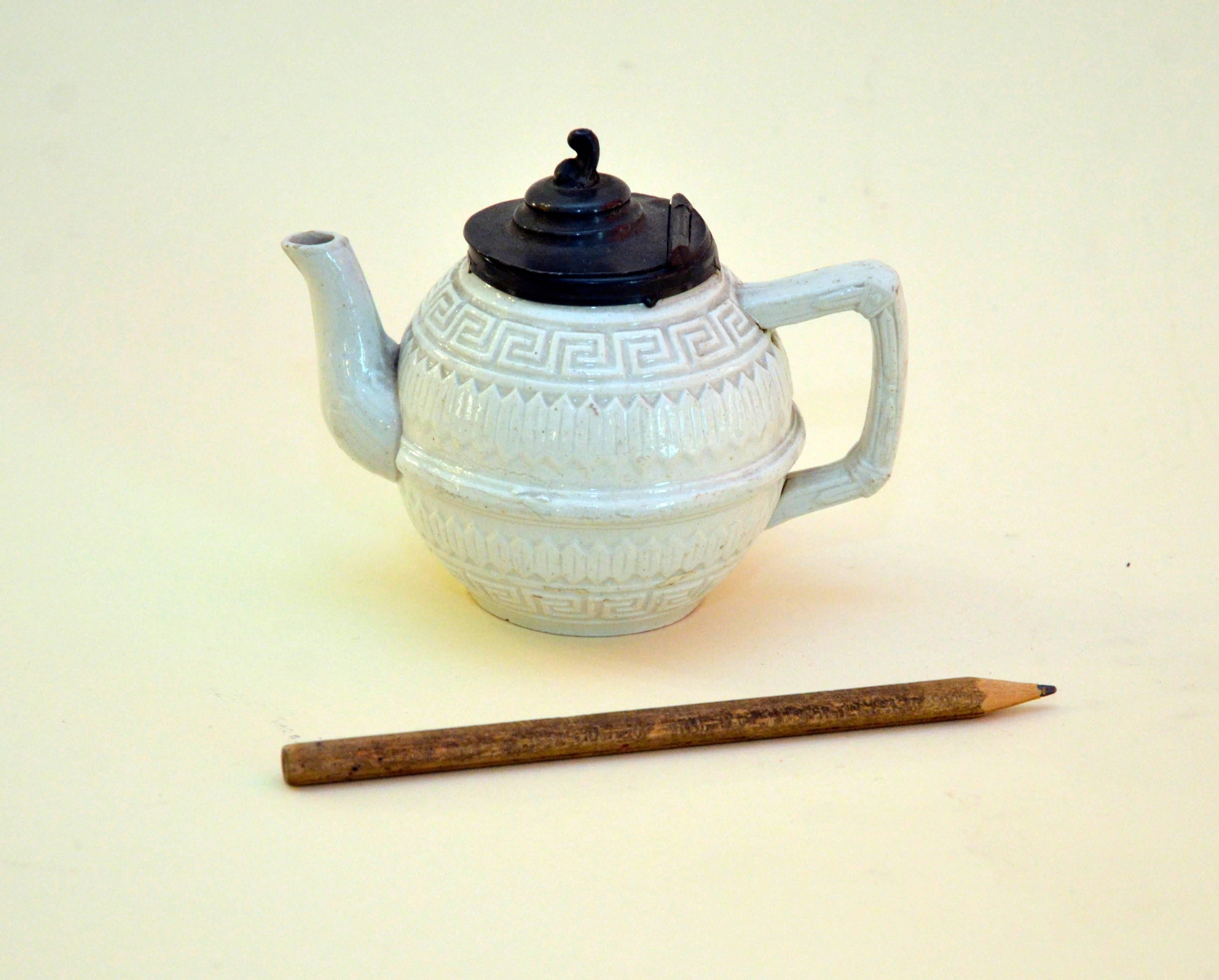 This salt glazed ironstone small teapot with a Greek geometric relief and lid made from pewter was realized in Staffordshire, England in 1860s-1870s. Adding salt to the kiln in fact creates a gleaming but transparent glaze and a smooth, slightly