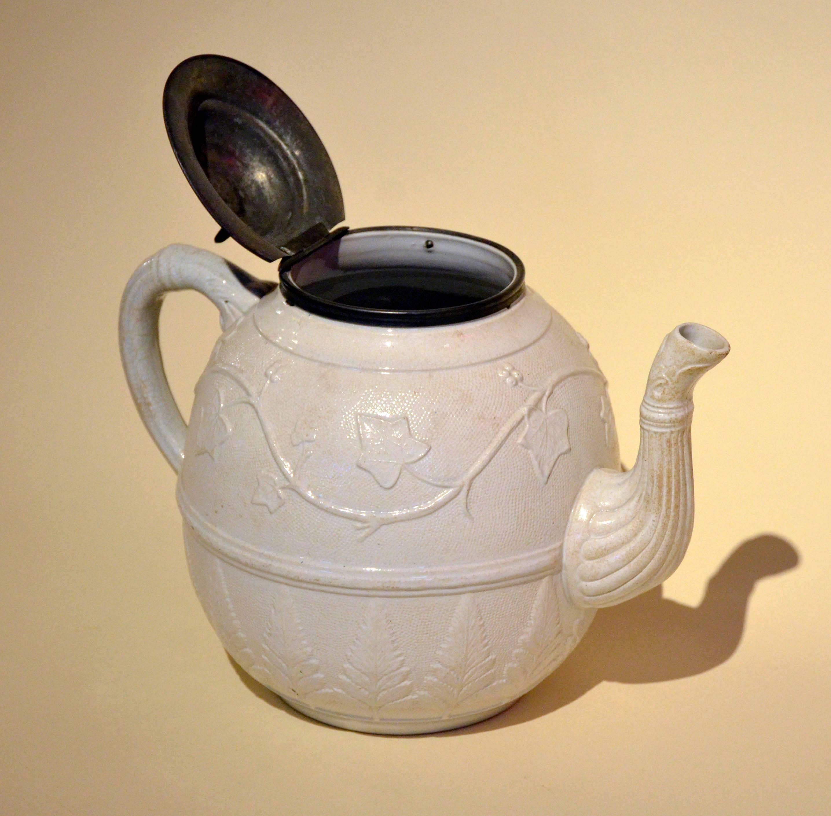 This very large salt glazed ironstone teapot with an Victorian ivy and ferns reliefs and lid made from pewter was realized in Staffordshire, England in 1860s-1870s. Adding salt to the kiln in fact creates a gleaming but transparent glaze and a
