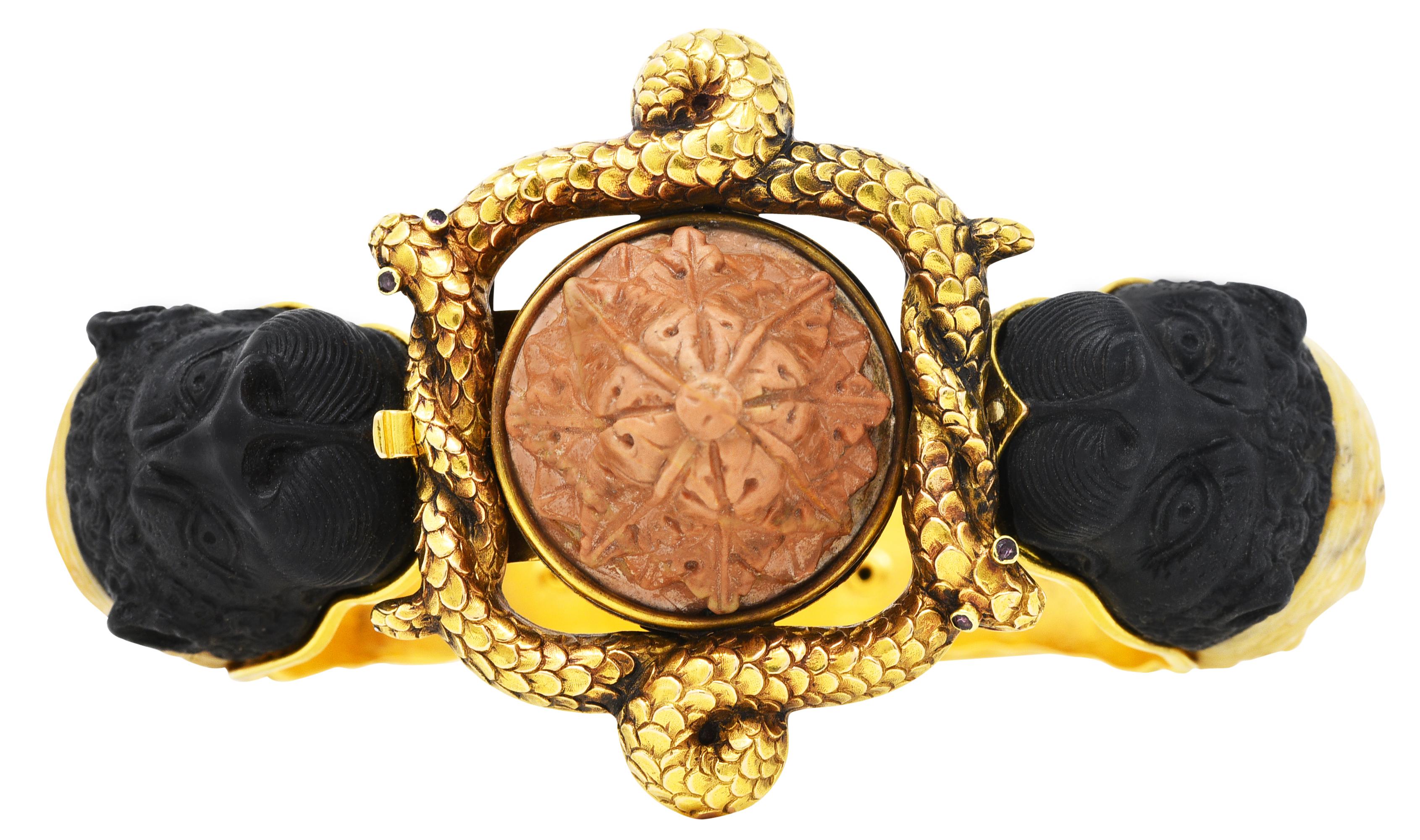 Hinged bangle bracelet features an ornately rendered snake love knot station

Eyes are bezel set with round cut and strongly purplish red gemstones

Centering pyramidal vegetable ivory deeply carved as foliate - opaque and light brown

Shoulders are