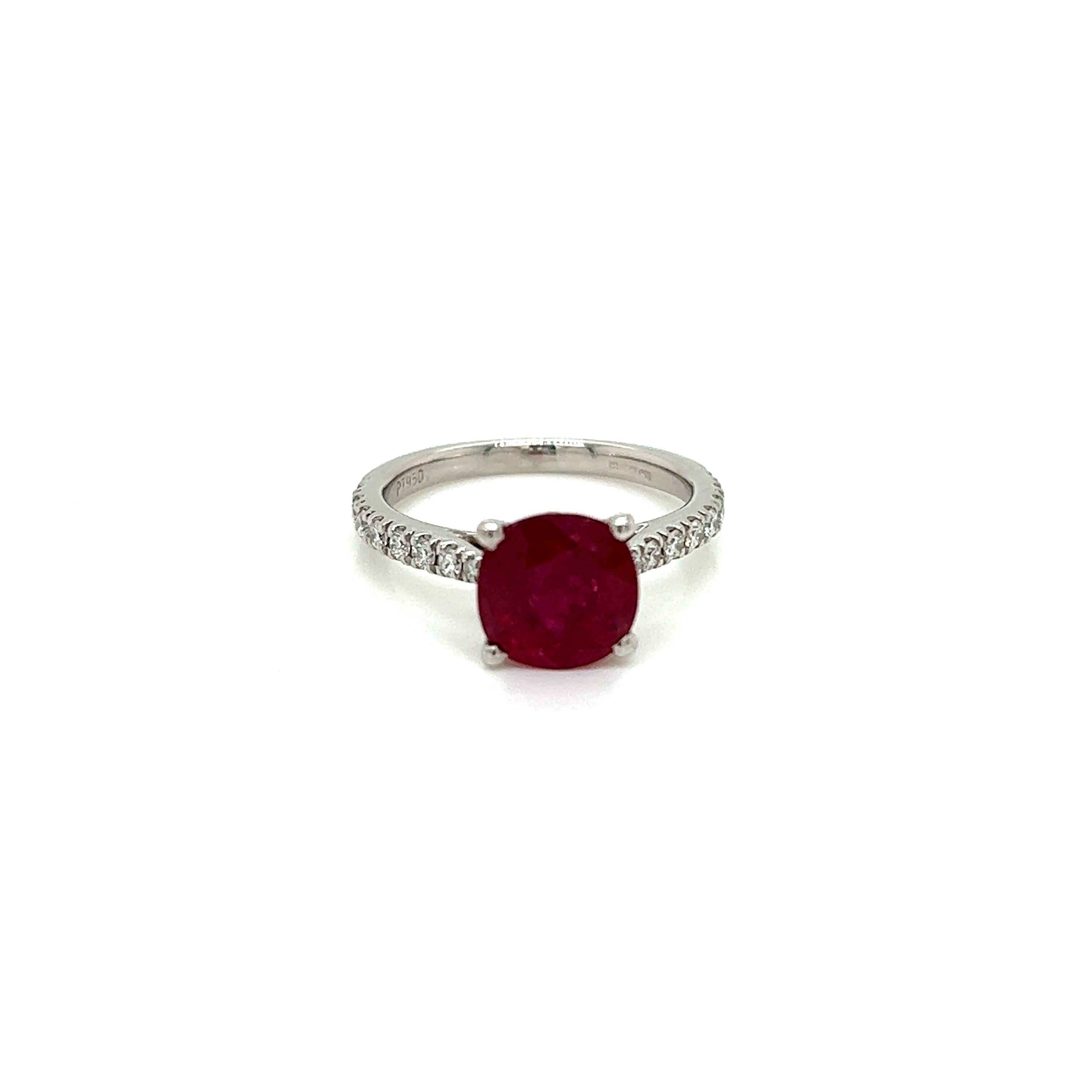 This alluring ring features a 1.87 Carat Ruby at its centre, held in a claw setting on a Diamond-encrusted Platinum band.  
The cushion cut Ruby is a rich, slightly pinkish red. Its deep hues are contrasted by the iridescent Diamonds accompanying it