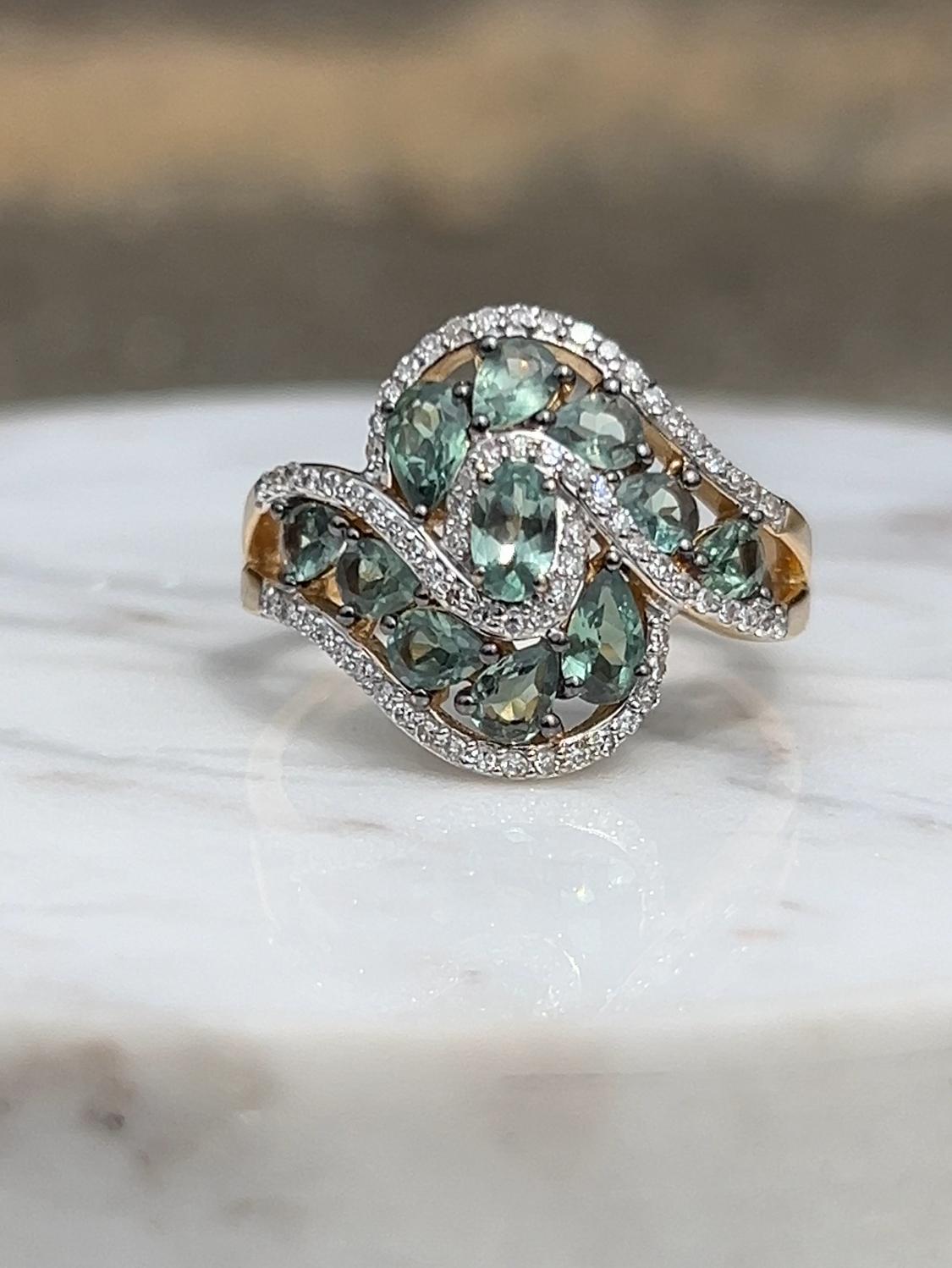 A striking contemporary bypass-style ring crafted in 14 karat yellow and white gold, showcasing the exceptional beauty of chrysoberyl. At its center glows a luminous 3x5mm oval chrysoberyl, gracefully accented by ten pear-shaped chrysoberyl