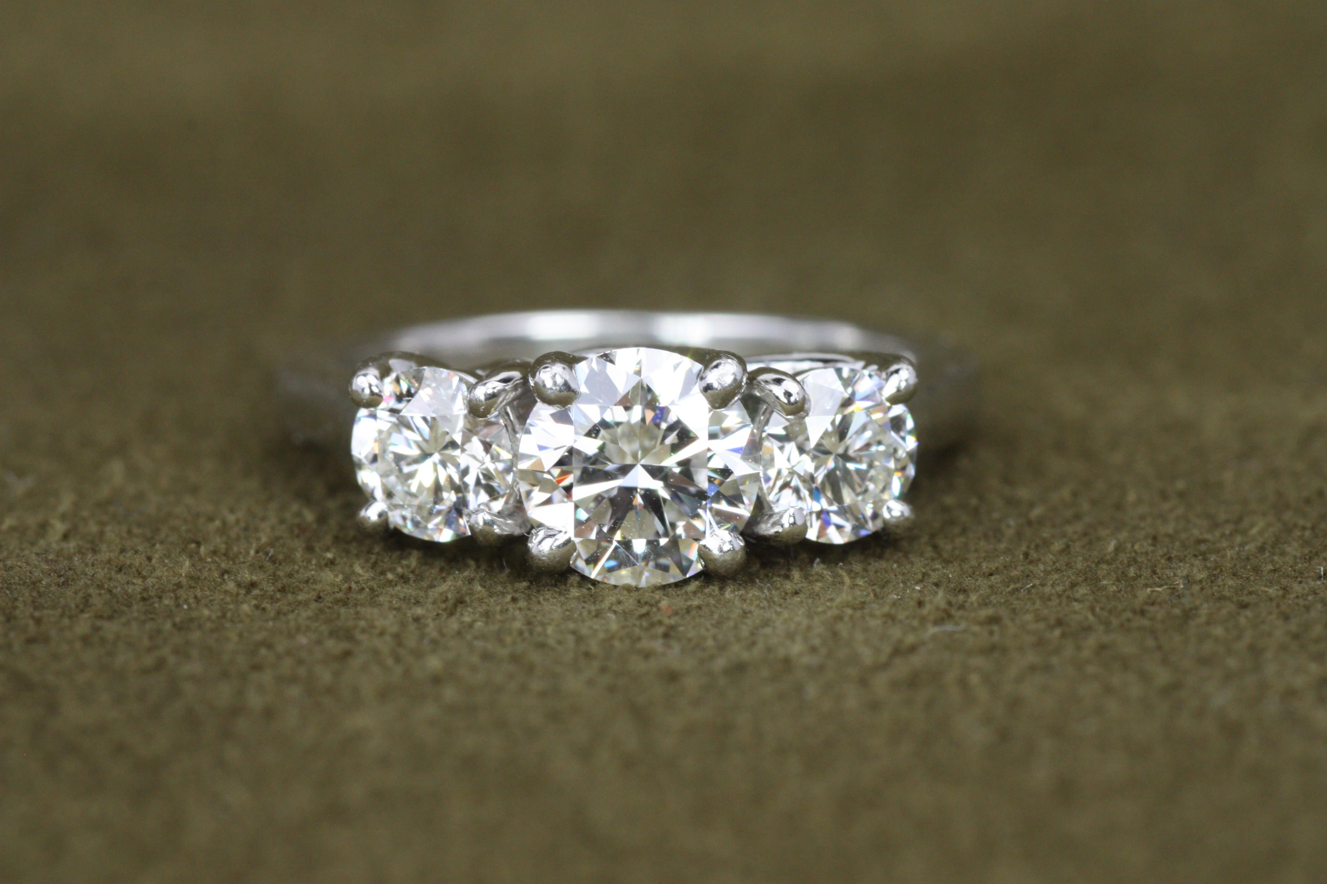 Cette magnifique bague de fiançailles en platine à 3 pierres met en valeur trois éblouissants diamants ronds de taille brillant, d'une valeur totale de 1,87ct. Le sertissage enveloppant ouvert rehausse l'éclat de chaque diamant, créant un aspect