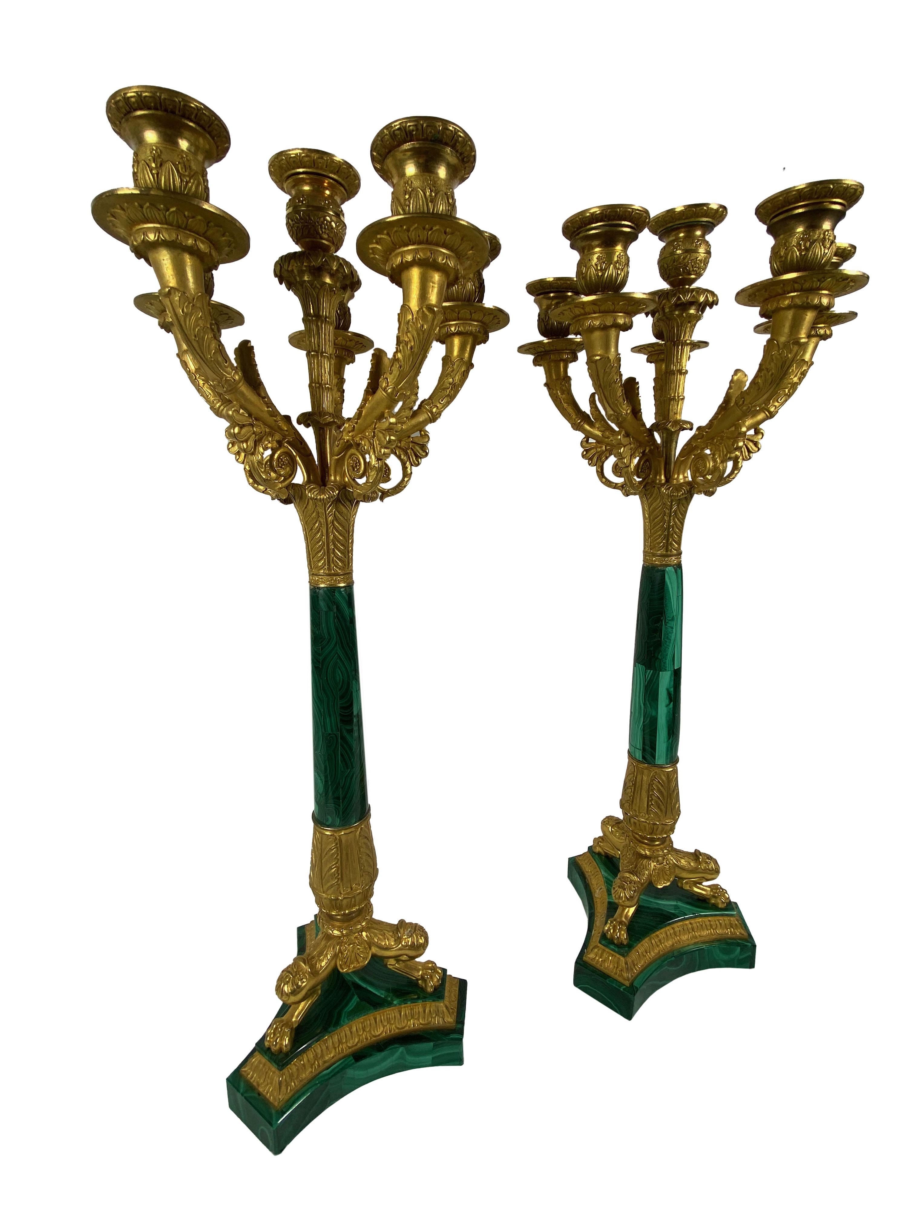 Una bella coppia di candelabri in bronzo dorato in stile Impero francese con steli affusolati in malachite che poggiano su tre piedi a zampa di leone su basi triformi in malachite. Circa 1870.
