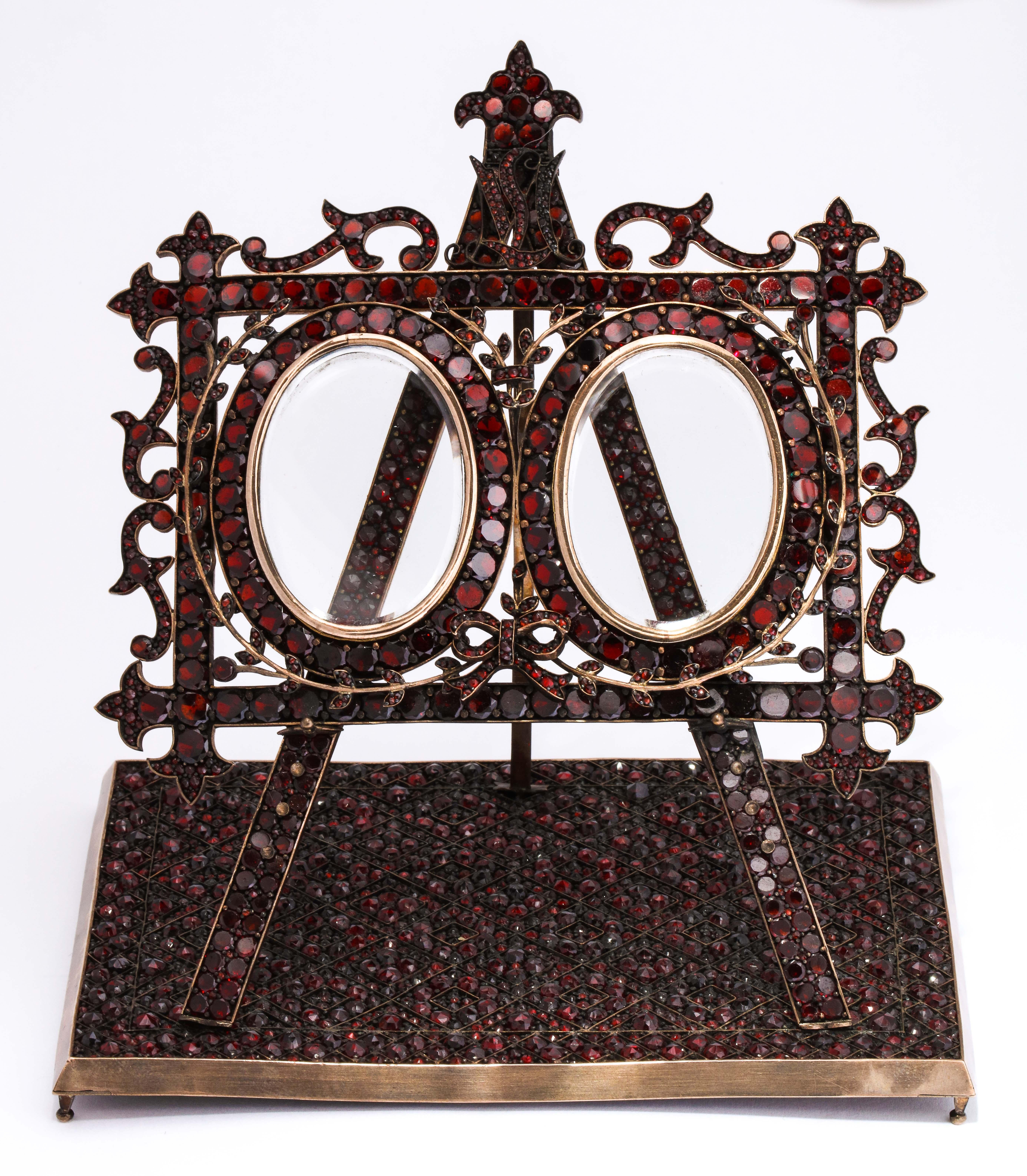  We offer you a luxurious and highly unusual 19th century double photo frame covered entirely with faceted Bohemian garnets designed as an easel standing on a geometric oriental carpet the oval openings holding beveled glass inserts. Customized with