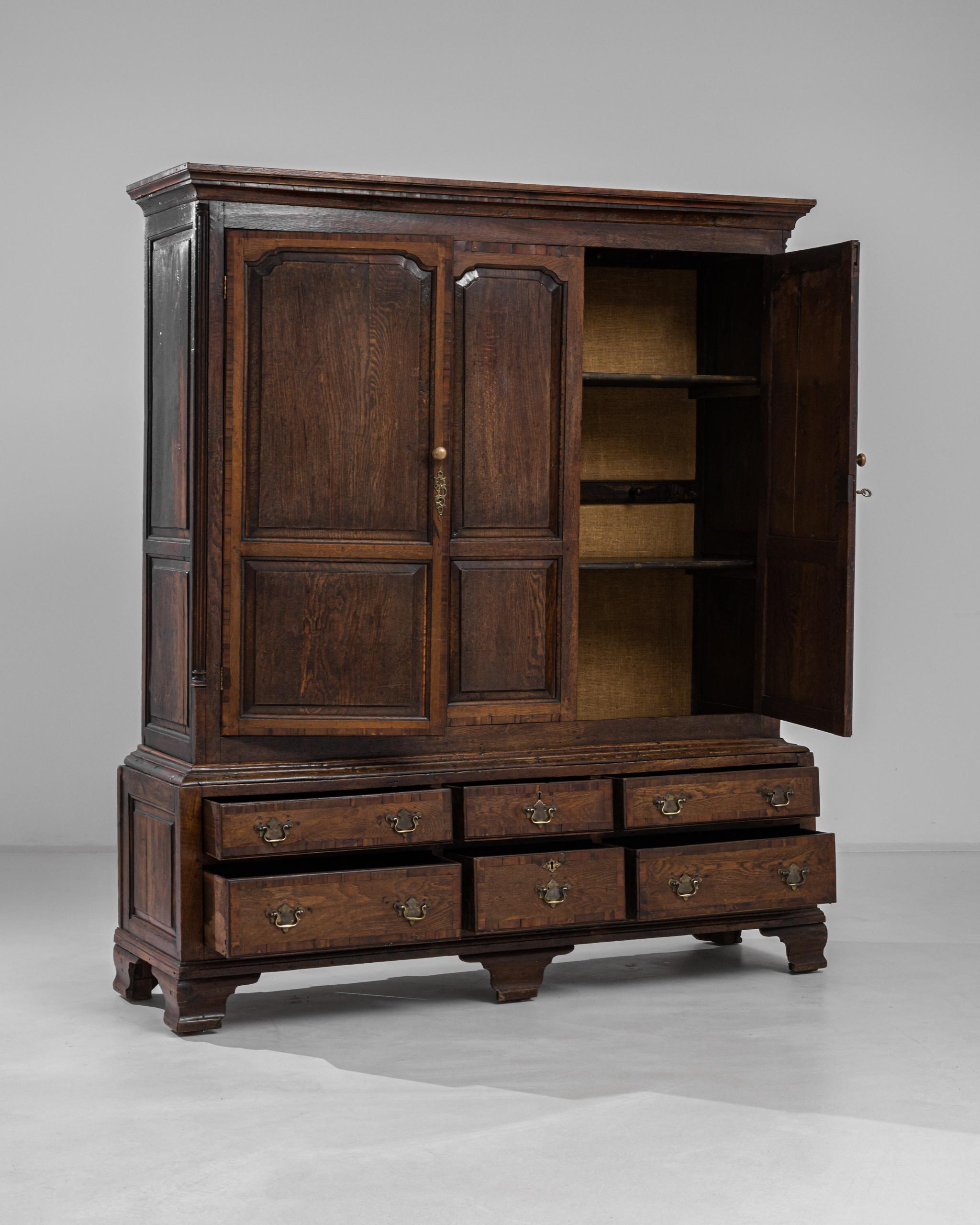 A dark wooden cabinet with brass hardware, circa 1870s England. Dark and warm oak panels comprise a large and elaborate structure. Lined with numerous drawers faced with an arch motif, this cabinet offers a sumptuous storage piece that will elevate