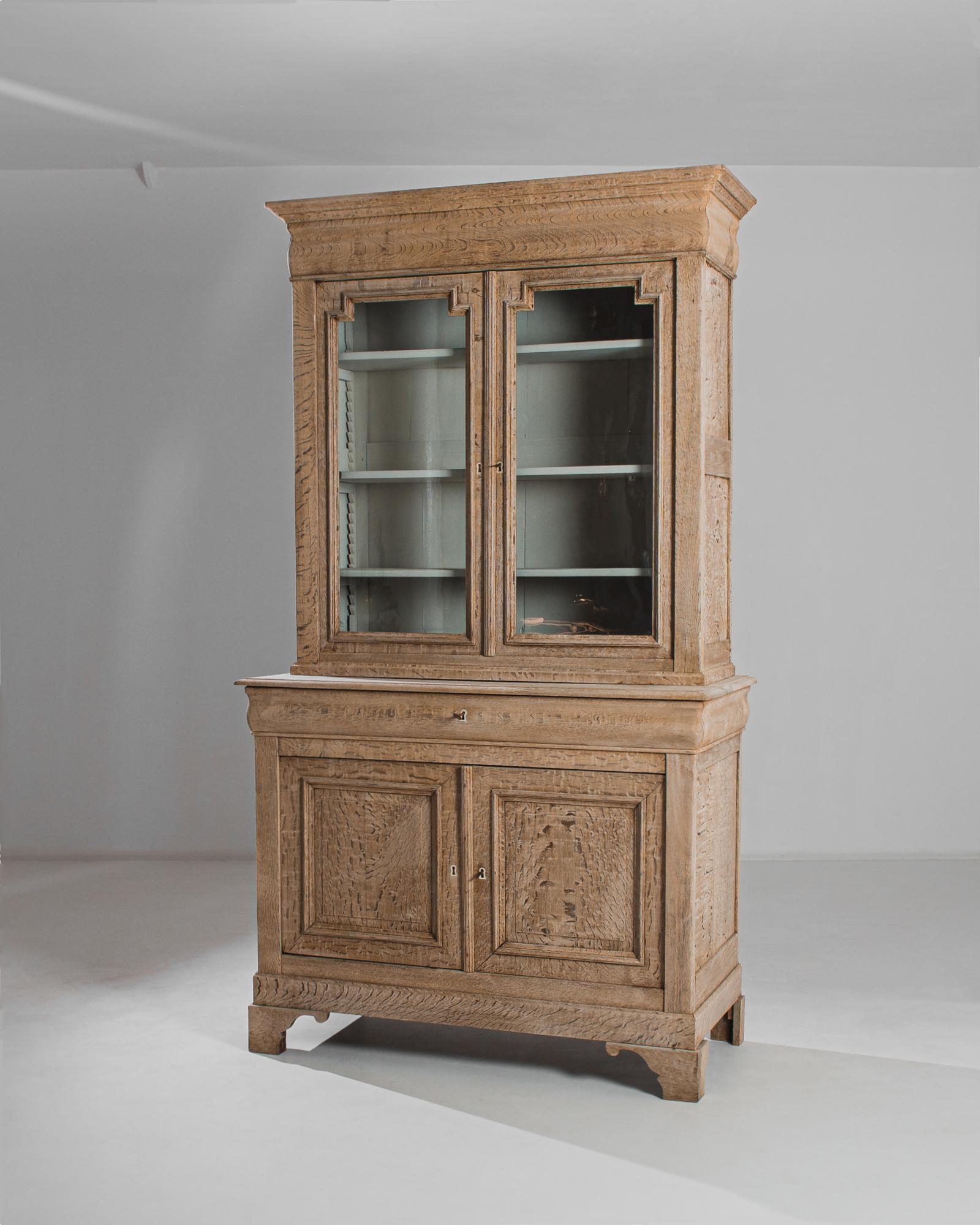 This bleached oak vitrine was made in France, circa 1870. Towering at over seven and a half feet, this monumental find strikes a presence in any setting. It features four shelves in the upper section with a fresh white interior, enhancing the rustic