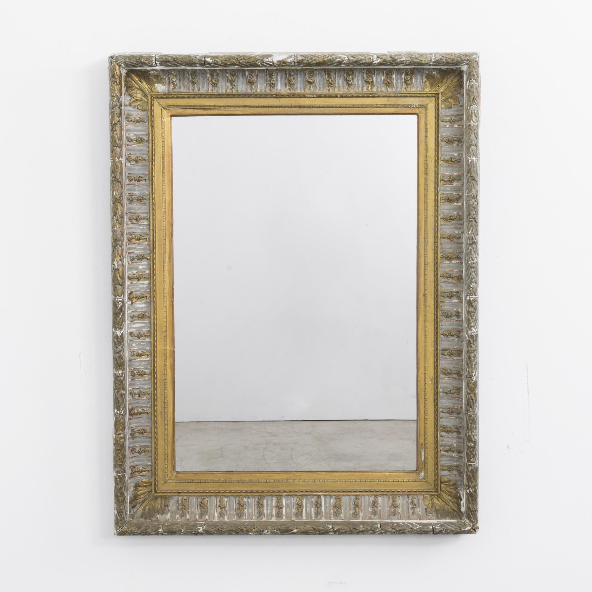 An antique gilded mirror from France, circa 1870. Elaborate filigree motifs — leaves, tulips, fleur de lis — scroll around the border of the frame. Age and patination create a range of tones, from pale gold to warm copper. A soft distortion in the