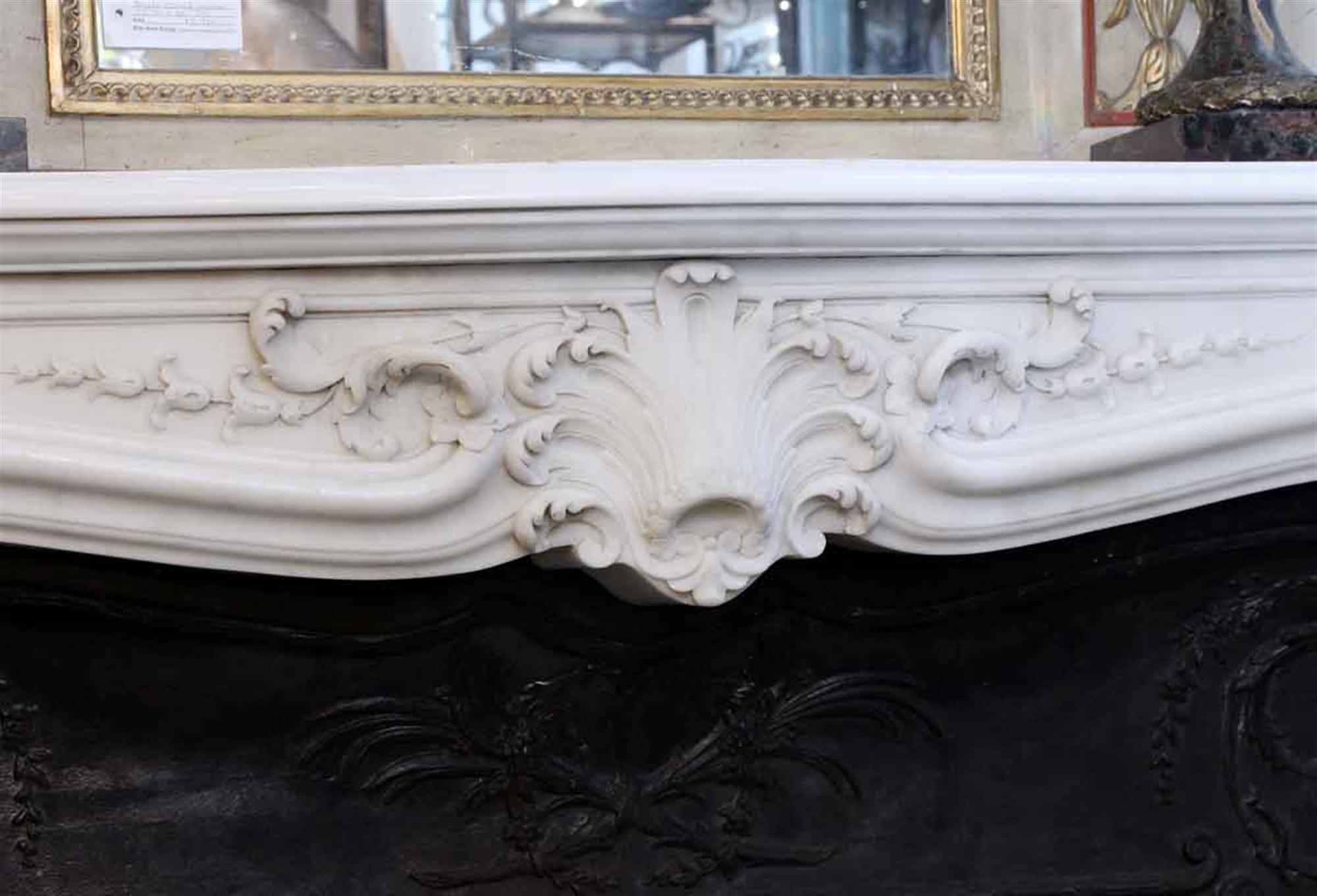 1870s beautifully detailed French white marble mantel with carved designs and over-the-top details at the keystone. A black decorative cast iron insert is included. Overall in excellent condition, but has one big scrape on the left leg and a few