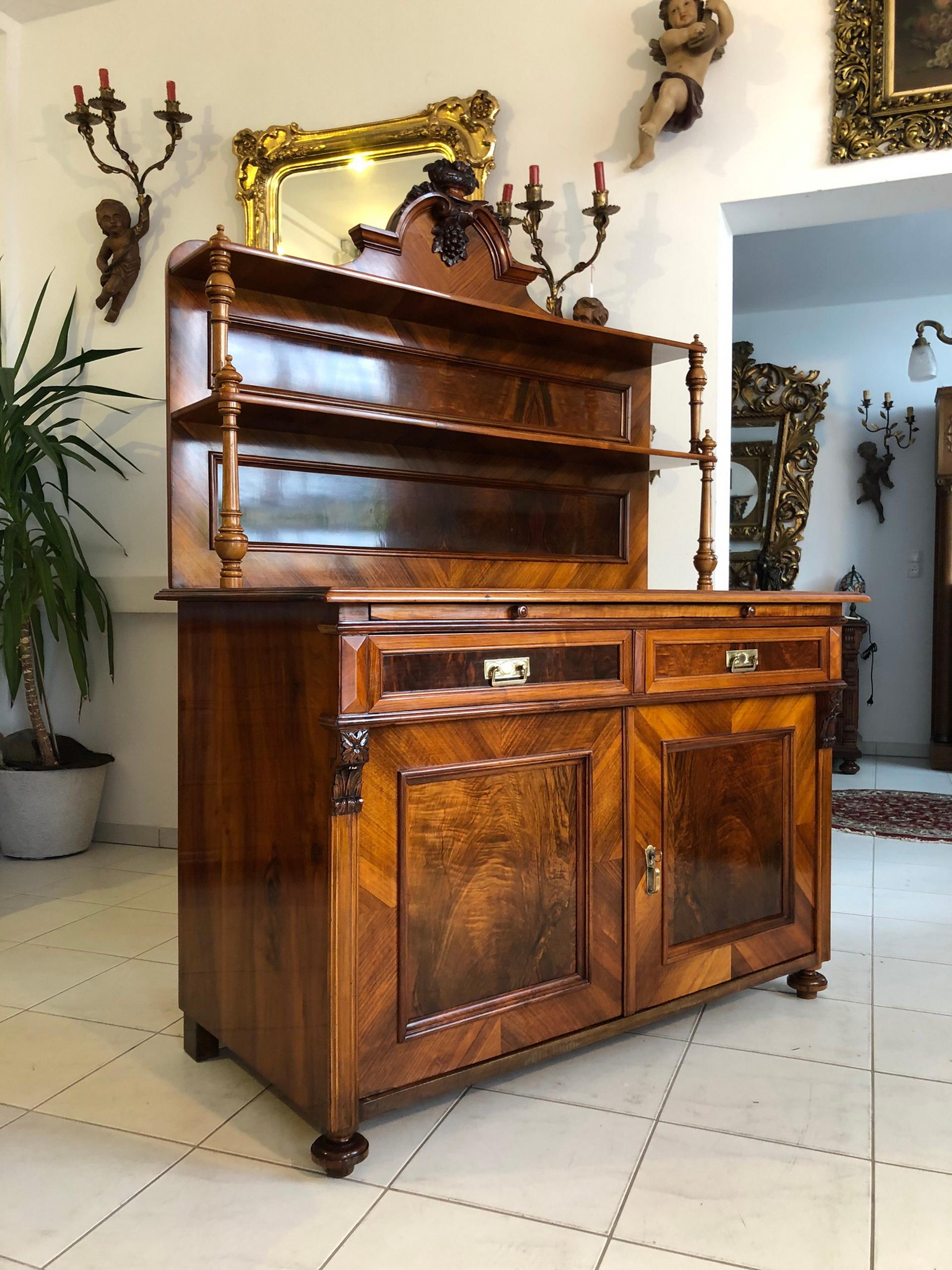 Antique historicism buffet from the late 19th century. Made out of walnut wood with a stunning warm brown veneer, this luxurious piece of furniture convinces with its compact measurements, yet plenty of closed and open storage space, as well as the