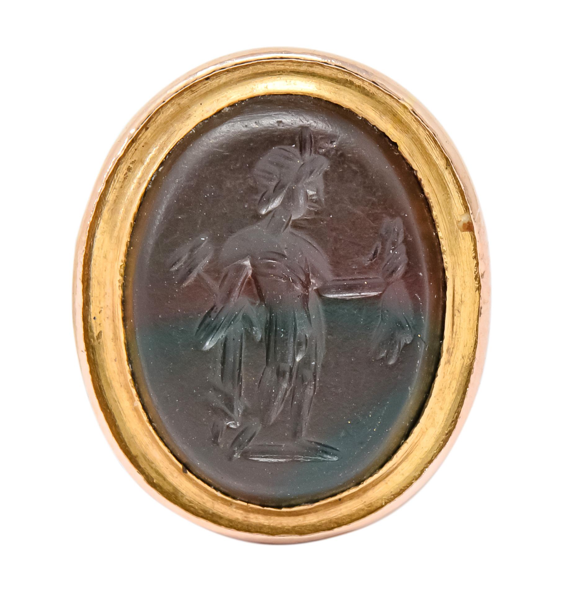 Featuring a hardstone intaglio seal depicting a standing figure with sash and articles held in hand 

Bezel set within a coiled serpentine 14 karat gold fob pendant that displays a textured scale motif

Circa 1870 

Tested as 14 karat