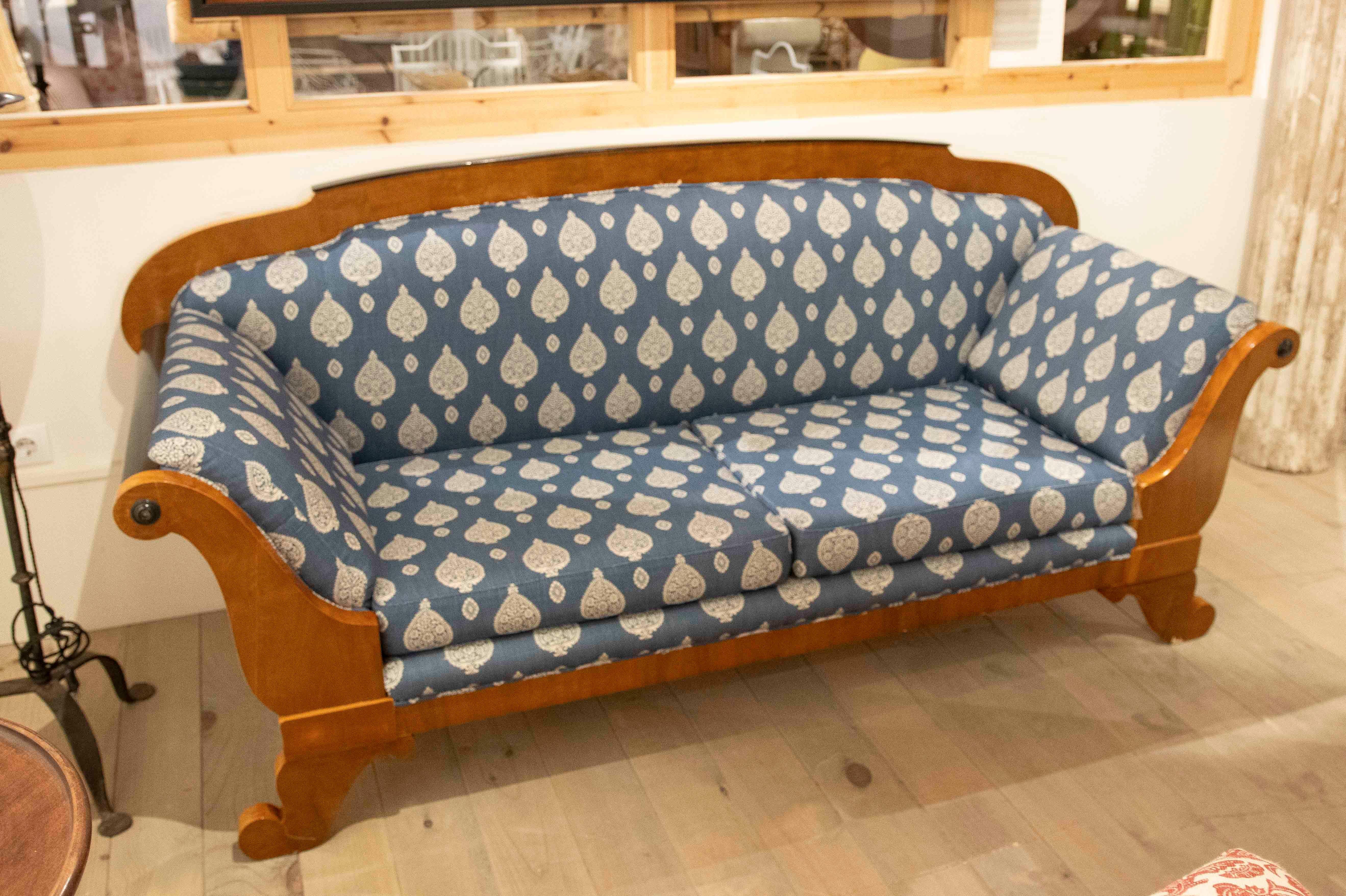 Elegante divano a tre posti con una struttura in legno dalla finitura calda e uno schienale dolcemente curvo. Rivestita in tessuto blu con tradizionali motivi floreali bianchi, offre un aspetto accogliente e distinto. Ideale per soggiorni classici,