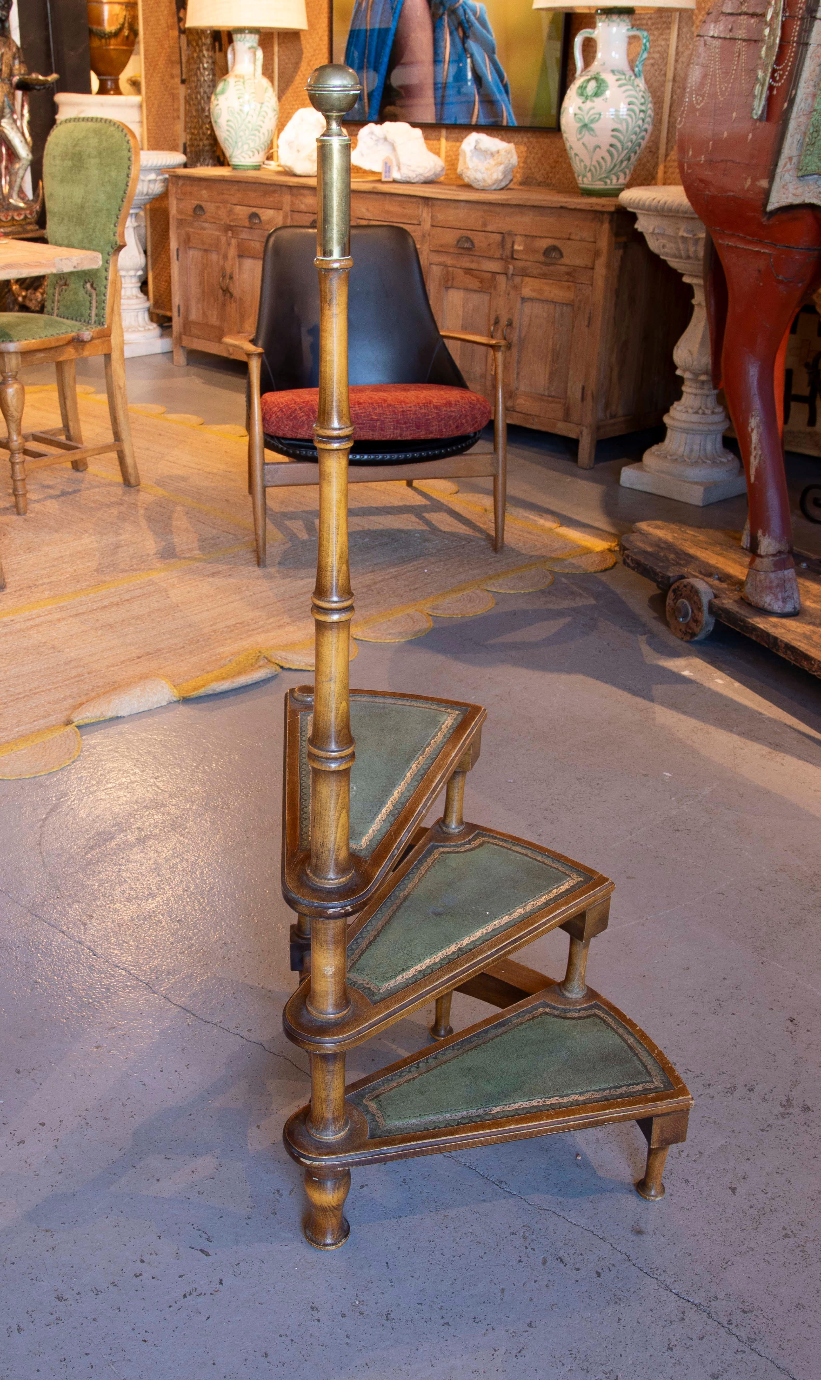 An elegant spiral library staircase, a functional and decorative piece ideal for interiors with character. Made of solid wood, this staircase stands out for its fan-shaped steps covered in aged green leather with embossed edges, giving it a refined