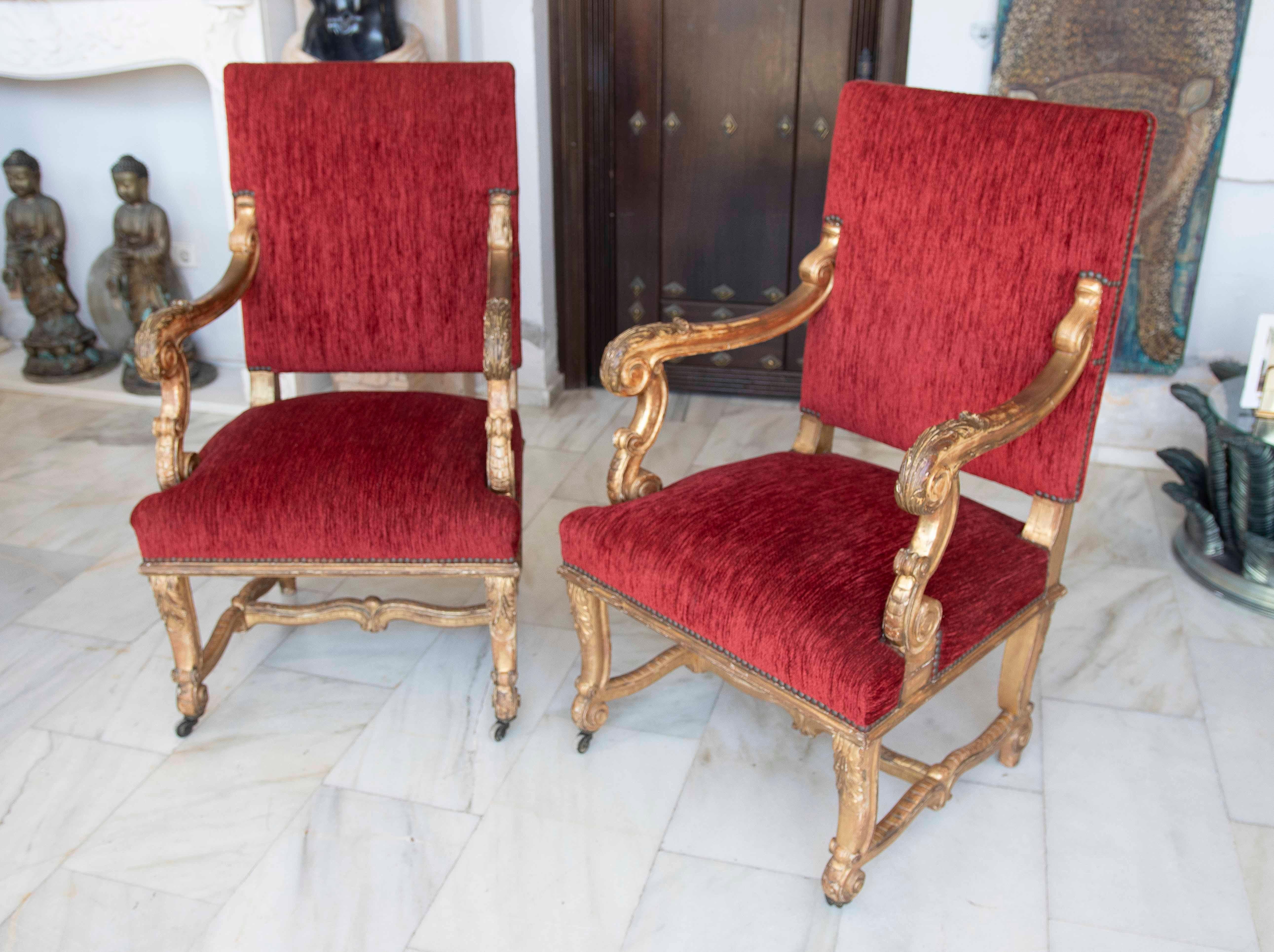 Elegante coppia di poltrone in stile Luigi XV, con struttura in legno intagliato e dorato a foglia, che mette in evidenza gli squisiti dettagli ornamentali sui braccioli e sulle gambe. Il suo lussuoso rivestimento in velluto rosso conferisce un'aria