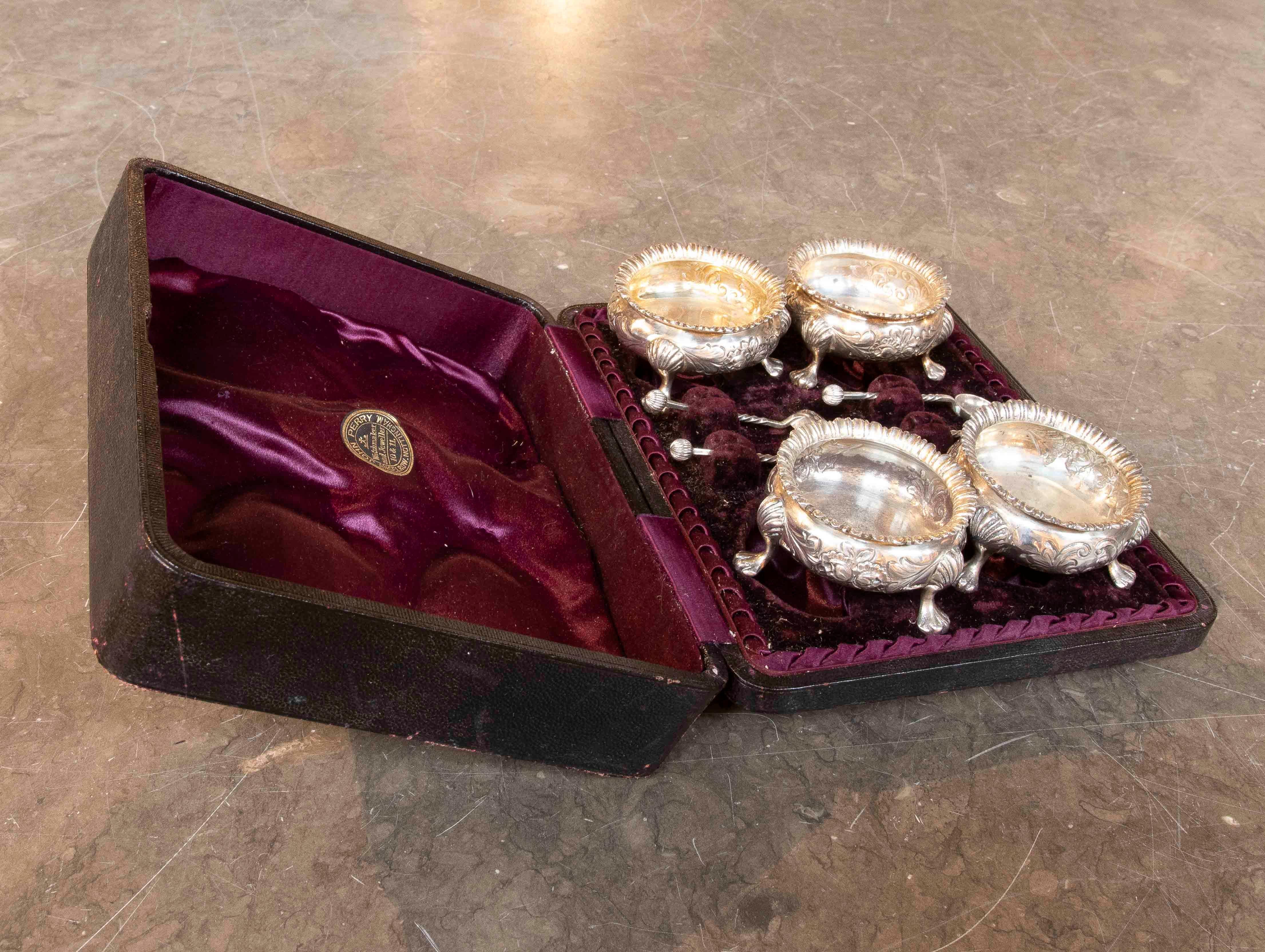 An exquisite Victorian silver salt cellar set, preserved in its original burgundy leather case with a wine-colored velvet and silk interior. The set includes four salt cellars and their corresponding teaspoons, all finely decorated with plant