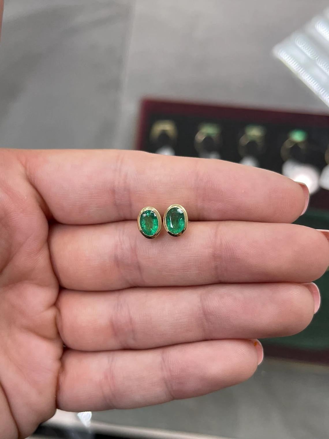 Displayed are gorgeous bezel set natural oval Zambian emeralds yellow gold bezel studs in 14K. These gold stud earrings are handmade by our expert jeweler and sparkle with an approximate total weight of 1.87 carats of natural emeralds. The gemstones